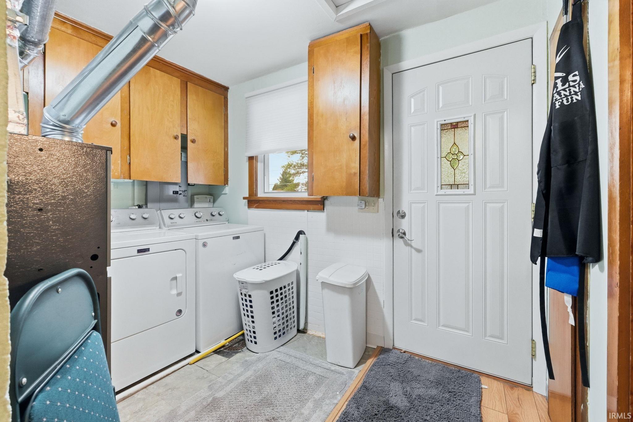 Dedicated laundry area featuring overhead wood-finish cabinetry, a white paneled door with a decorative glass insert, and a window with natural wood trim