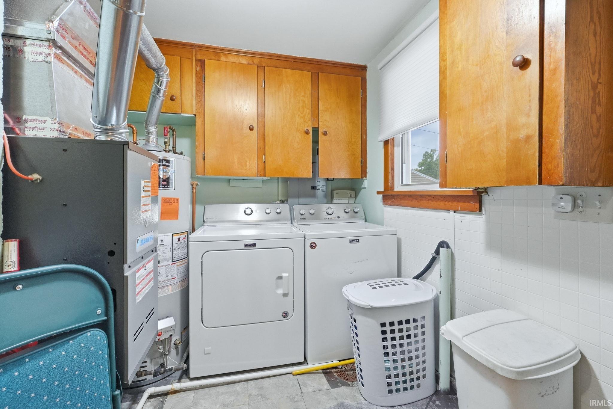 Dedicated laundry area featuring a window with a cellular shade, upper wood-finish cabinetry, and white tile wainscoting