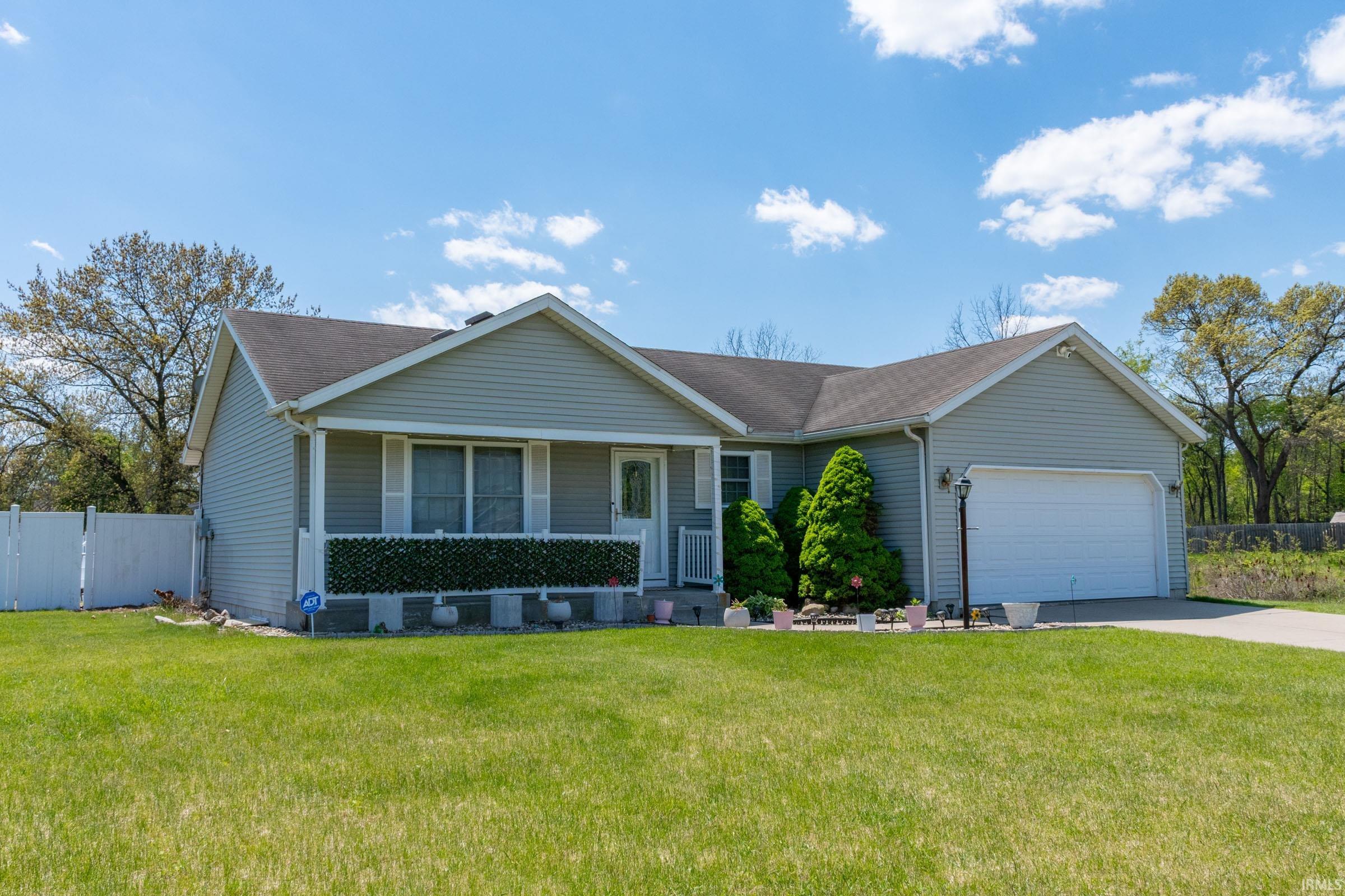 Ranch-style residence featuring light grey siding, an attached garage, and a covered front porch