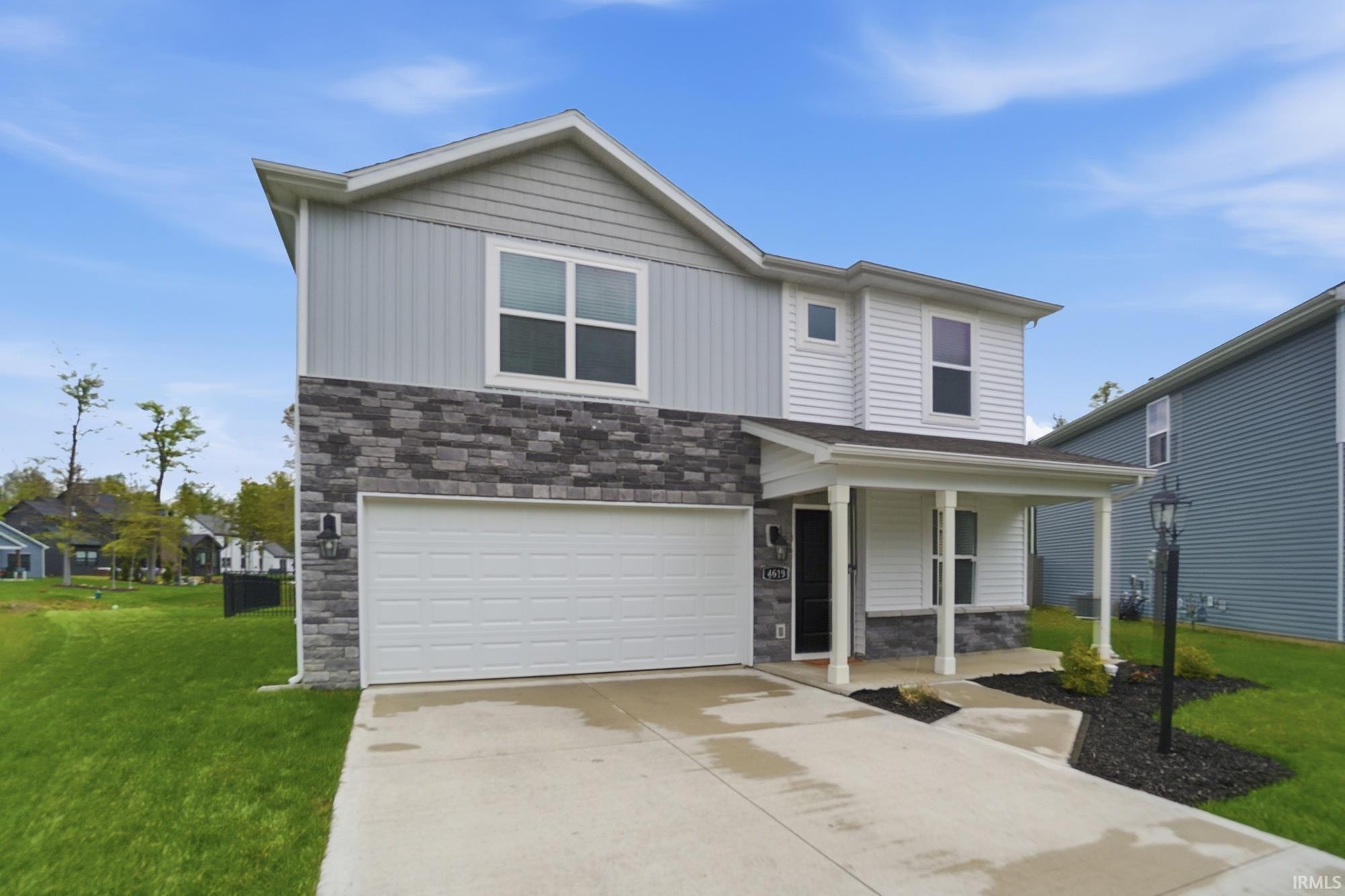 Contemporary two-story exterior featuring a covered entry porch, mixed siding and stone veneer accents, an attached garage, and a concrete driveway