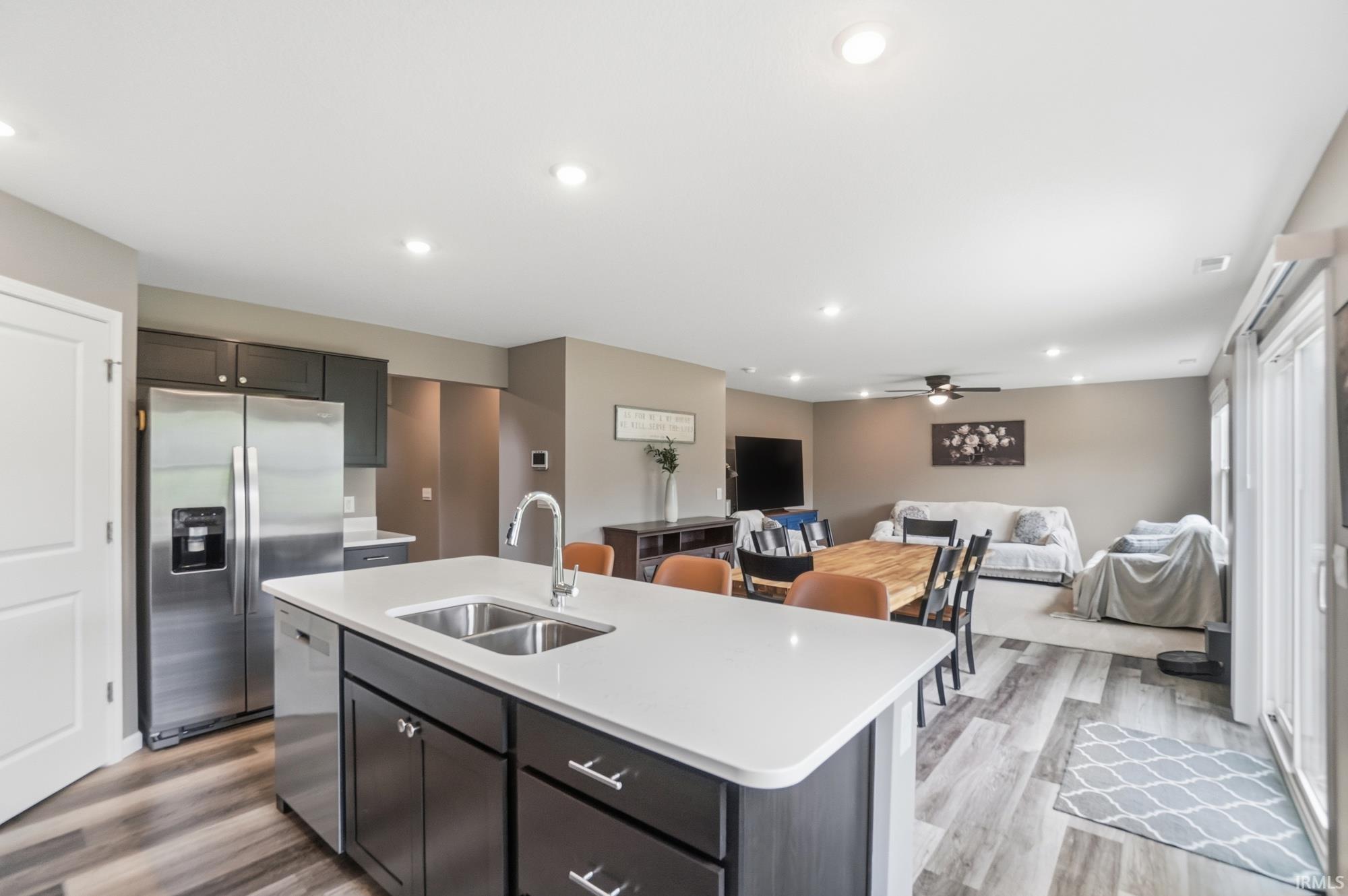 Open-concept living space featuring a central kitchen island with a double basin sink, stainless steel appliances, wood-finish flooring, and recessed lighting