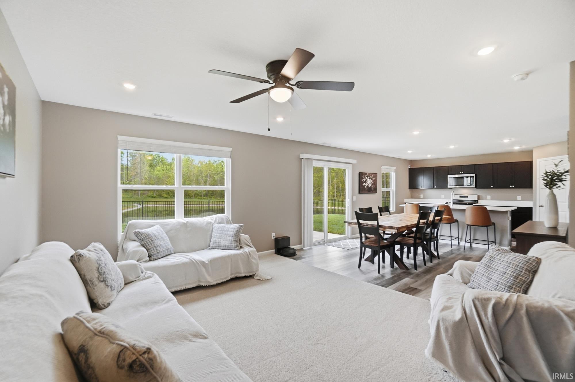 Open-concept living area featuring a ceiling fan, recessed lighting, and a large window overlooking a wooded area