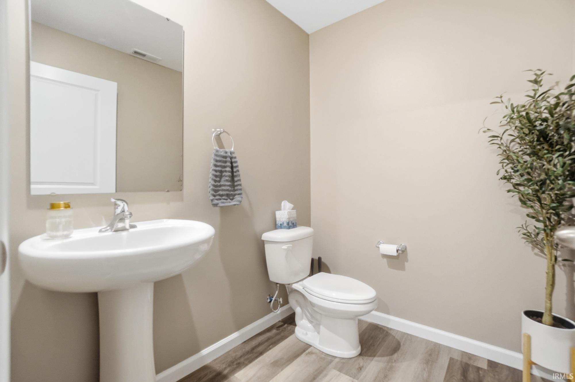 Pedestal sink with chrome faucet, a white toilet, and wood-finish flooring