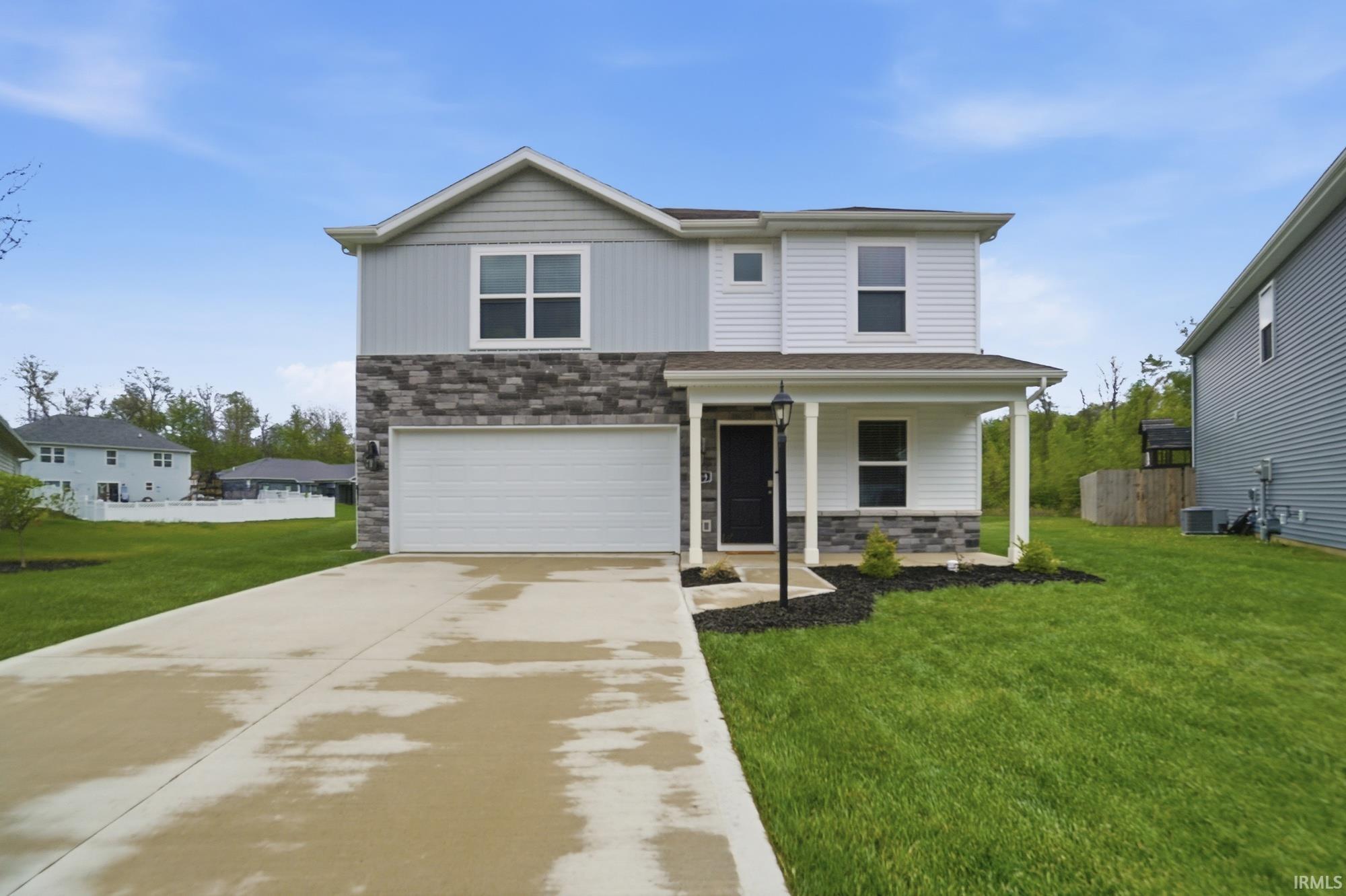 Two-story residence featuring a covered front porch, a two-car garage, and a multi-textured facade with stone accents and siding