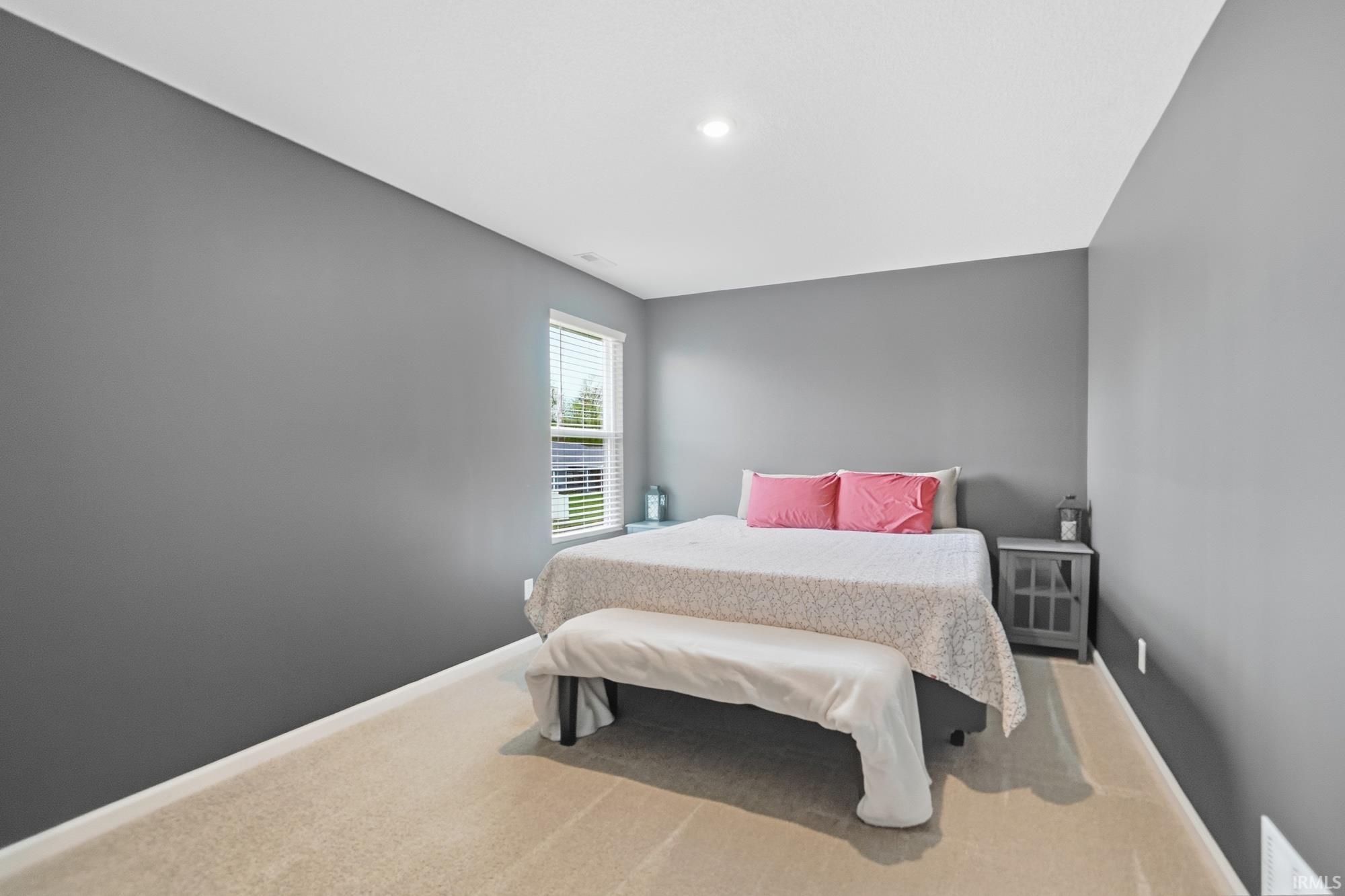 Carpeted room with a single window featuring blinds, a ceiling-mounted light fixture, and neutral gray walls