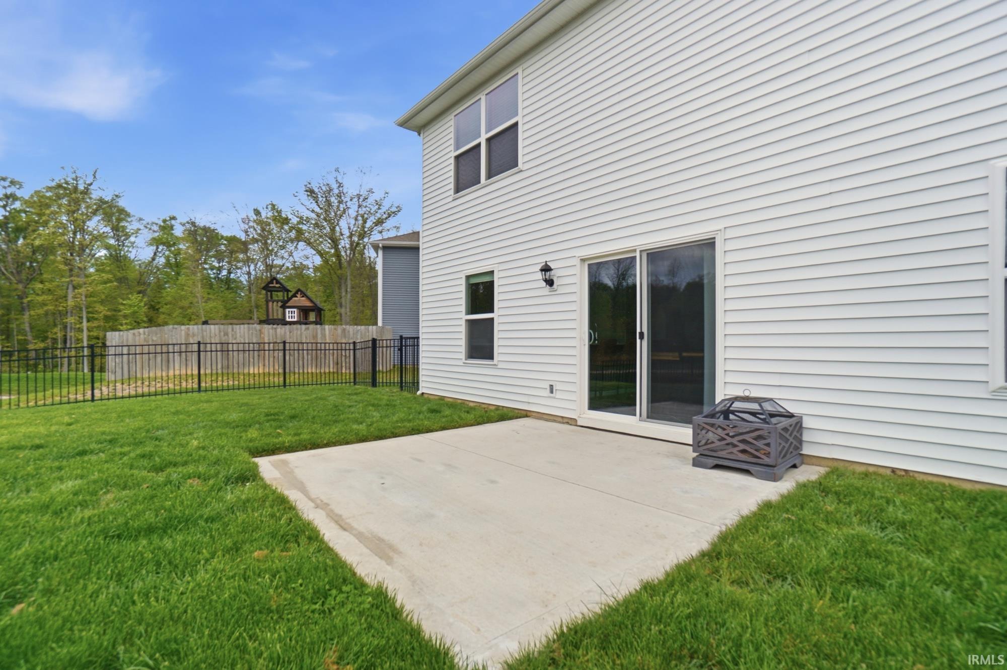 Rear patio featuring a concrete surface, sliding glass door access, white horizontal siding, an exterior wall light, and a fenced yard with natural landscaping