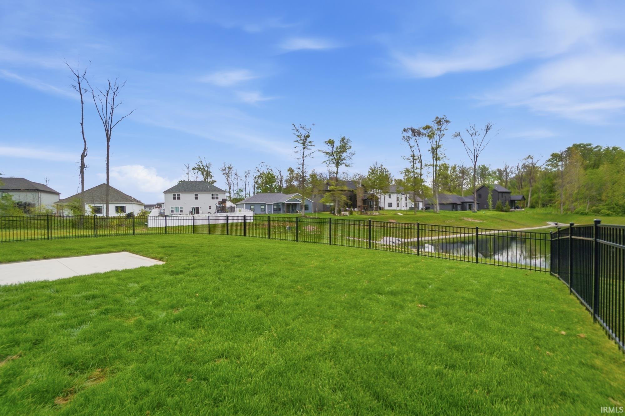 Expansive green lawn featuring a concrete patio pad and black metal fencing