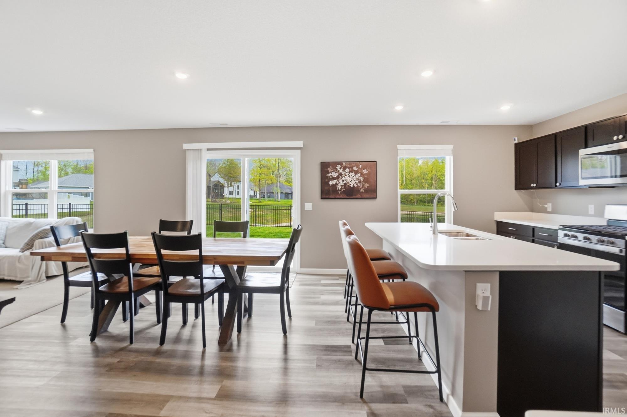 Open-concept living area featuring wood-finish flooring, a contemporary kitchen island with a built-in sink, dark cabinetry, and stainless steel appliances