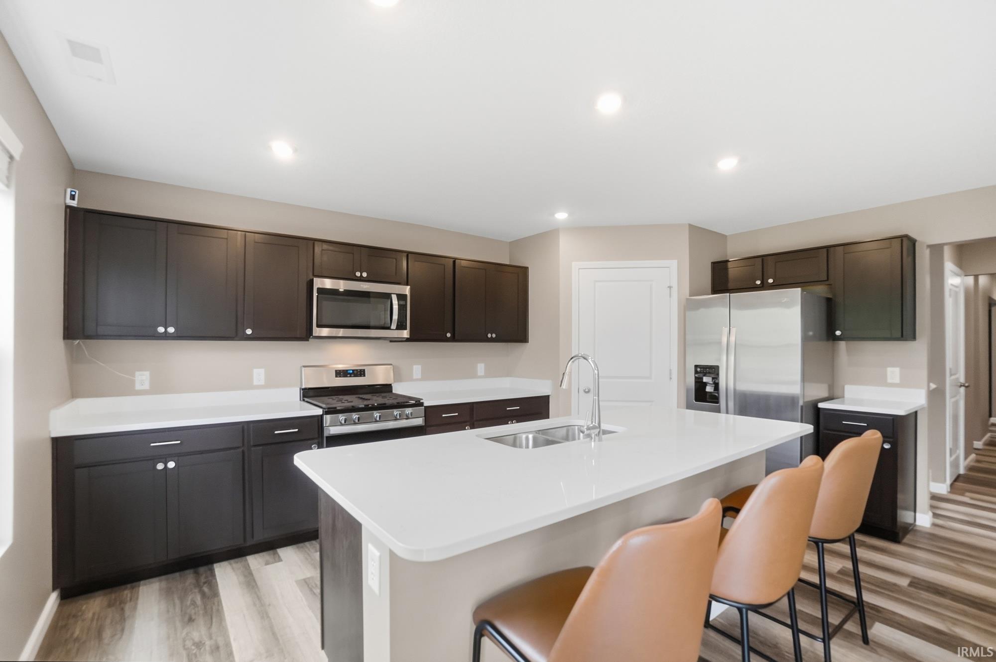 Contemporary kitchen featuring dark wood cabinetry, stainless steel appliances, a center island with a double basin sink, and wood-finish flooring