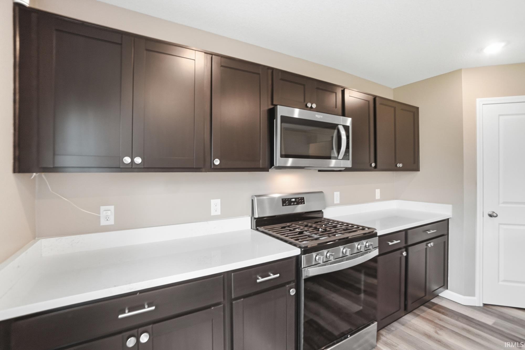 Kitchen featuring dark wood-finish cabinetry, white countertops, stainless steel gas range, and an over-range microwave