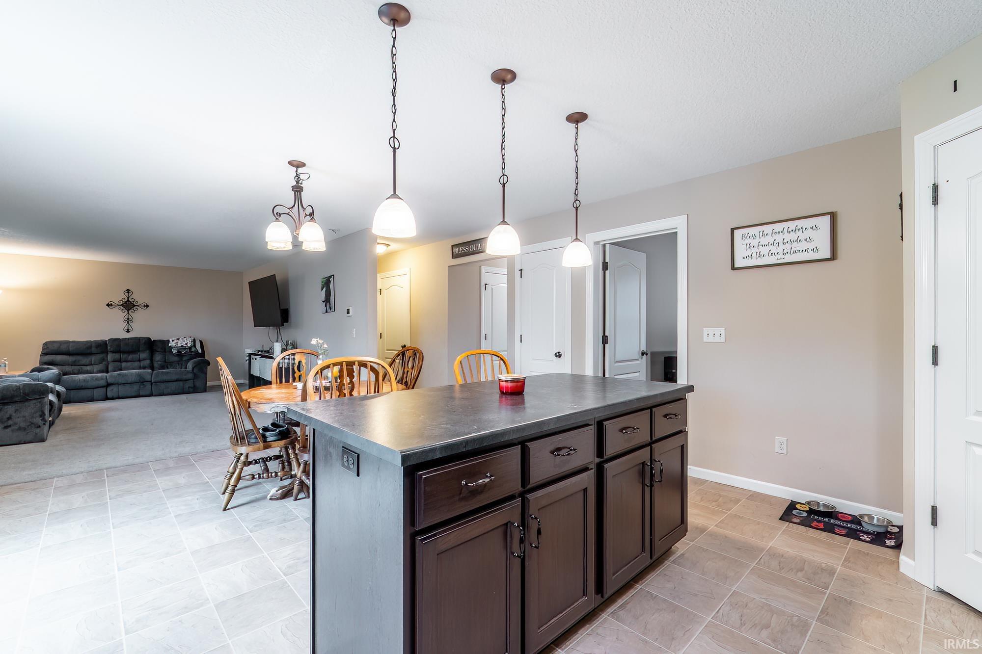 Kitchen island with dark wood cabinetry and a dark countertop, illuminated by three pendant lights