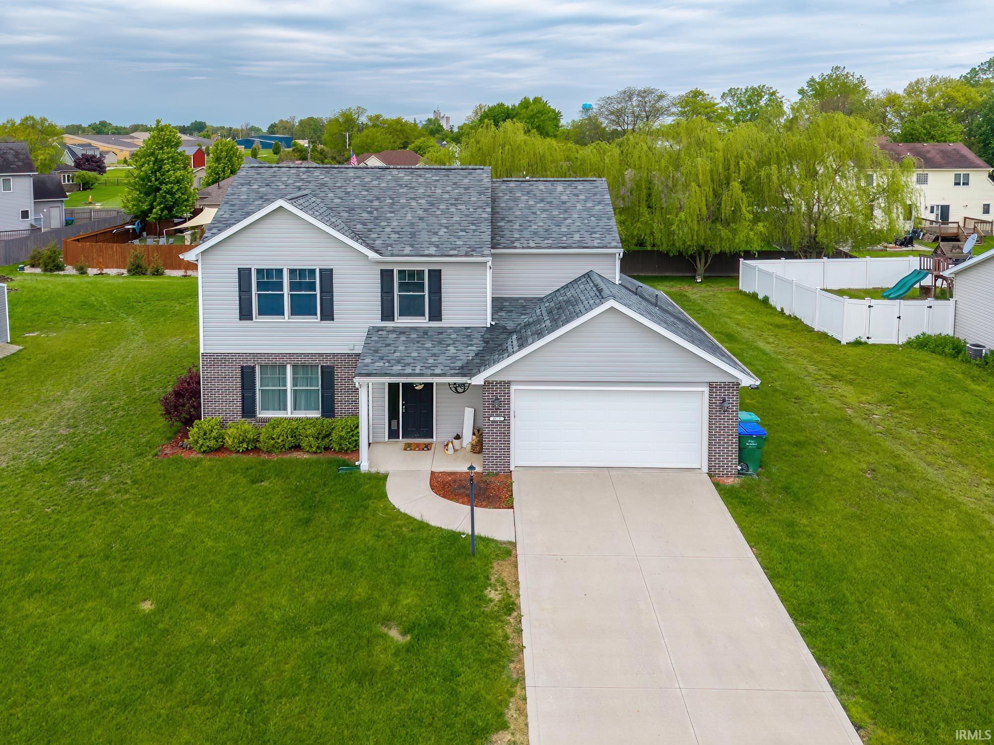 Two-story residence featuring light gray siding with brick accents, an attached garage, a paved driveway, and a front walkway