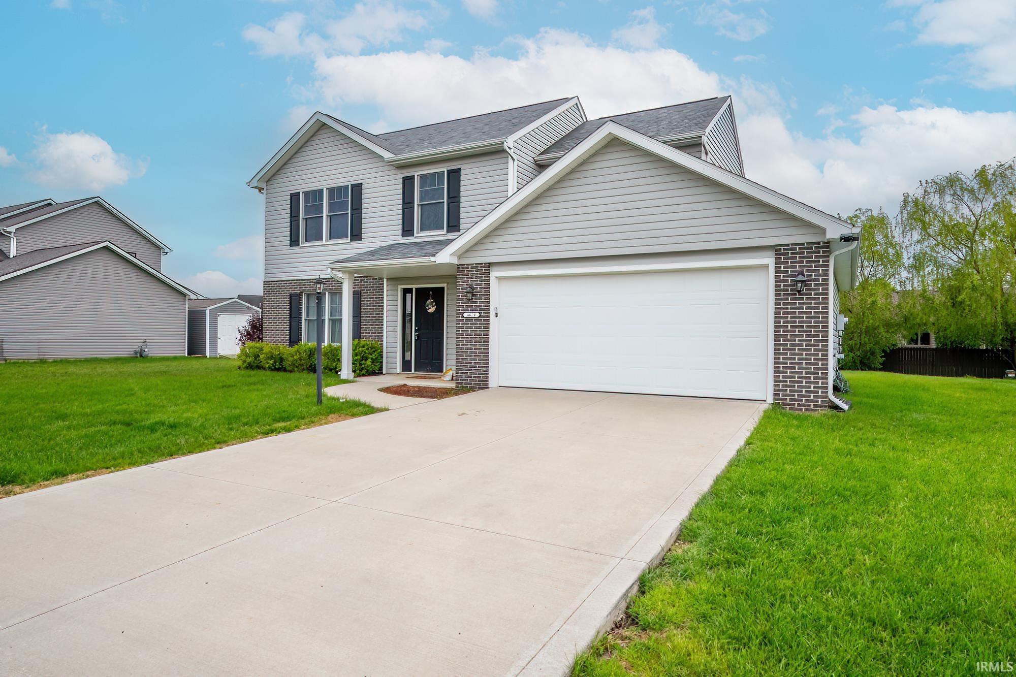 Contemporary two-story residence featuring light gray siding, dark gray brick accents, a two-car garage, and a concrete driveway