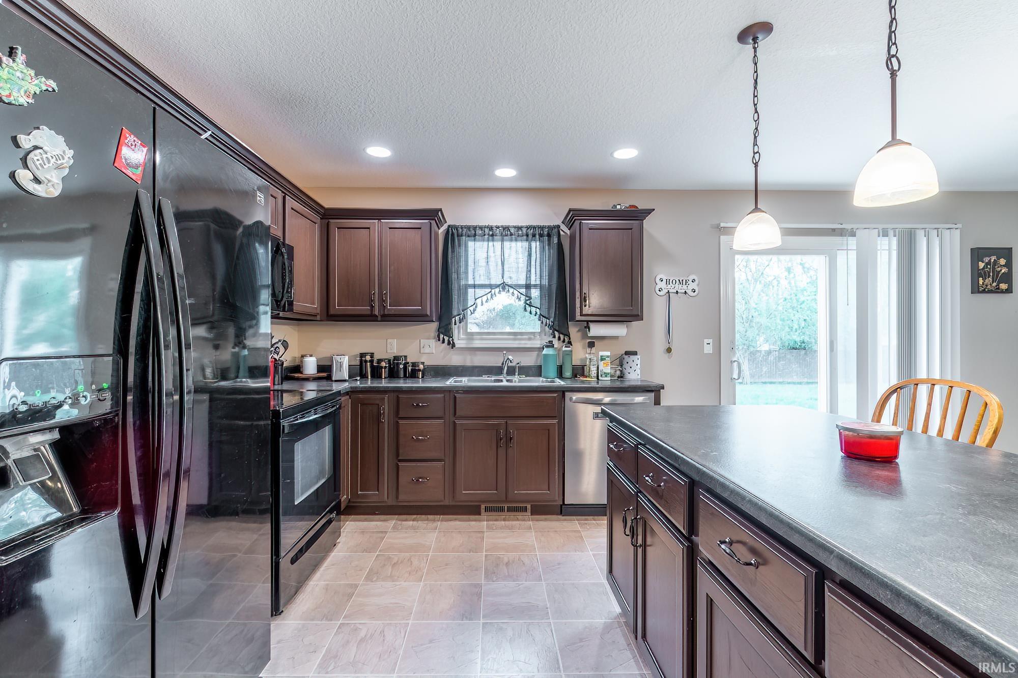 Kitchen featuring dark wood cabinetry, a large kitchen island with counter seating, stainless steel dishwasher, black appliances, and recessed lighting