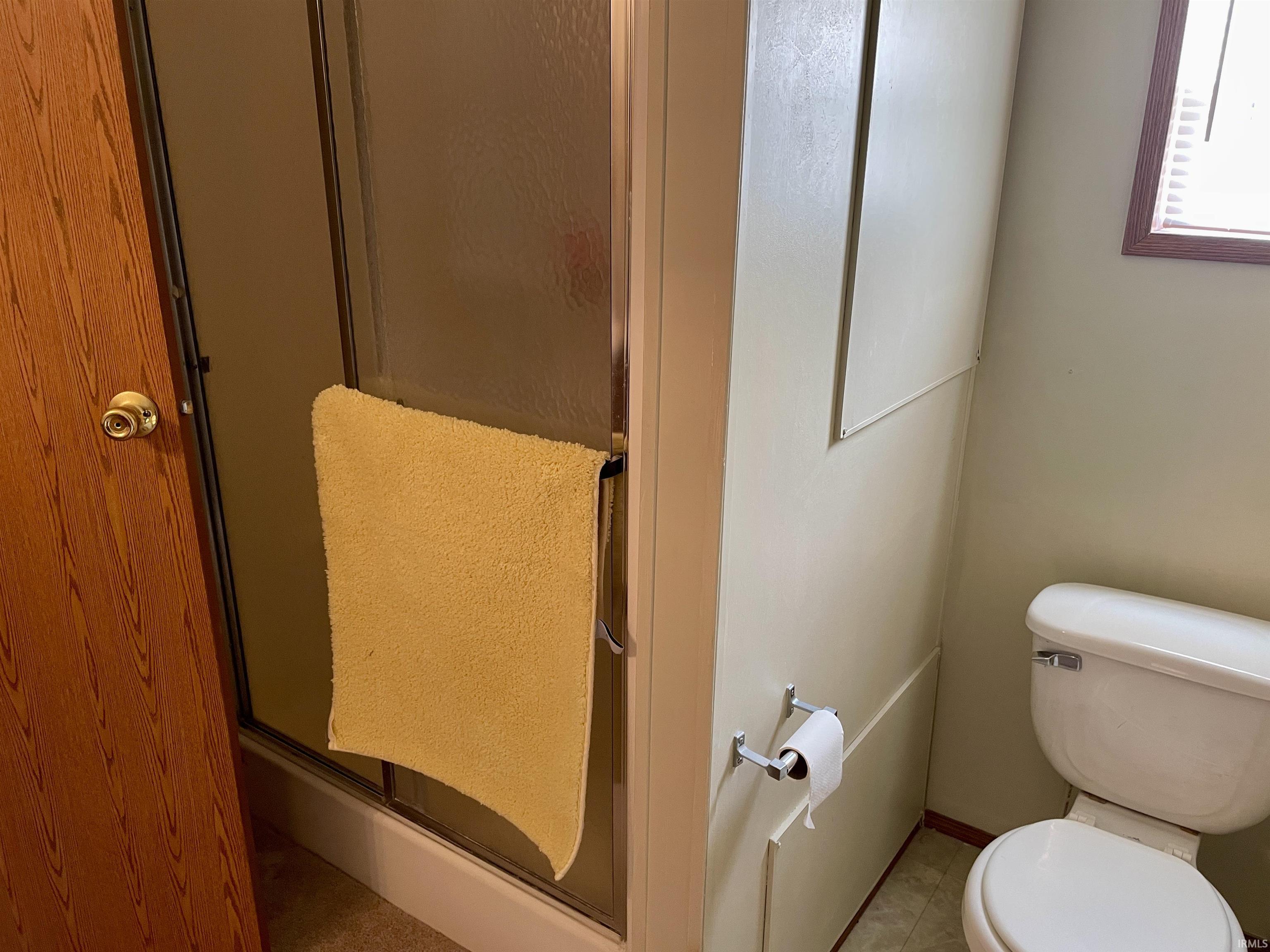 Shower enclosure with frosted glass door, light-colored paneling, and a white toilet