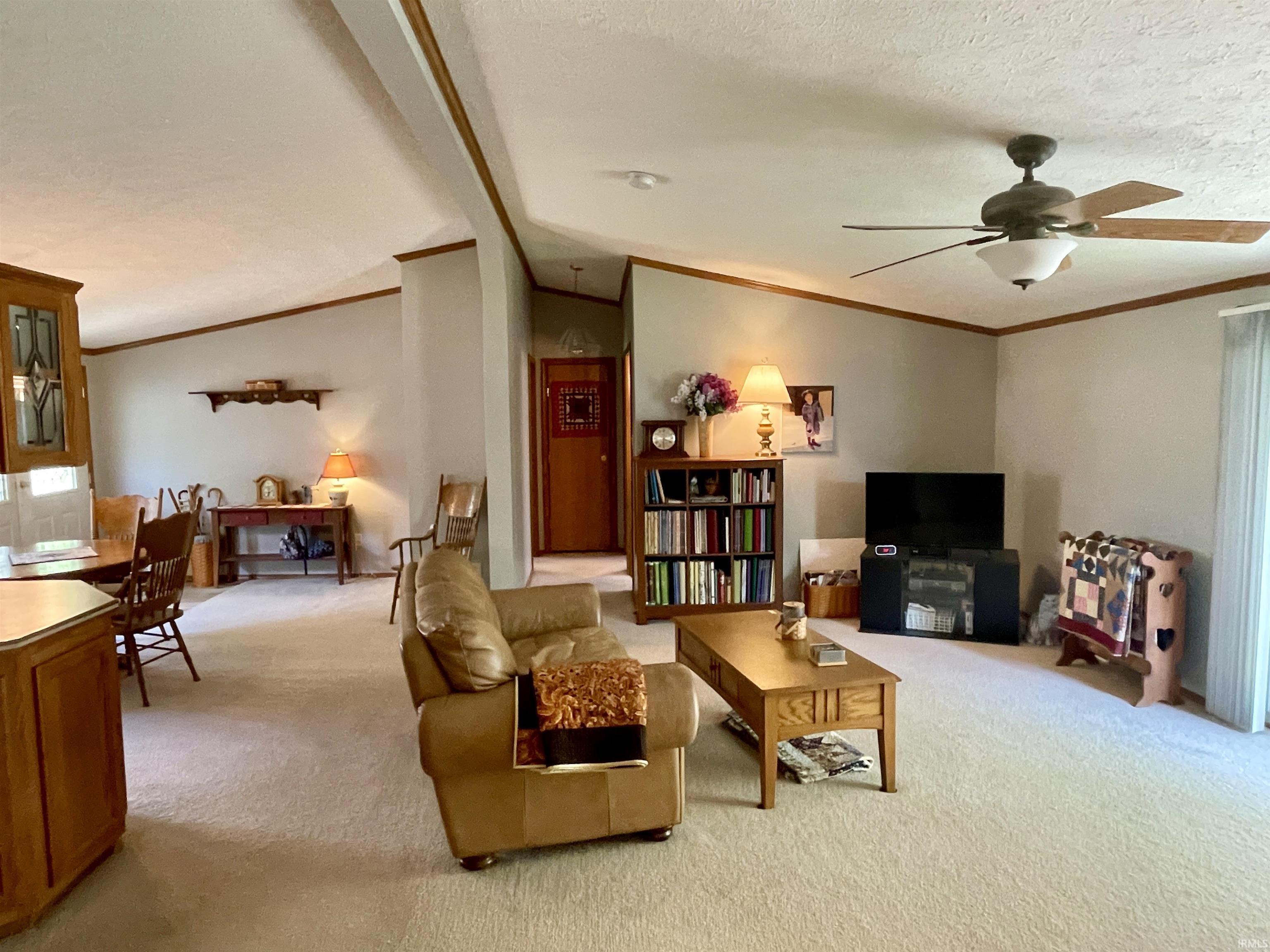 Spacious living area featuring vaulted ceilings with decorative wood trim, neutral carpeting, and a ceiling fan with integrated lighting