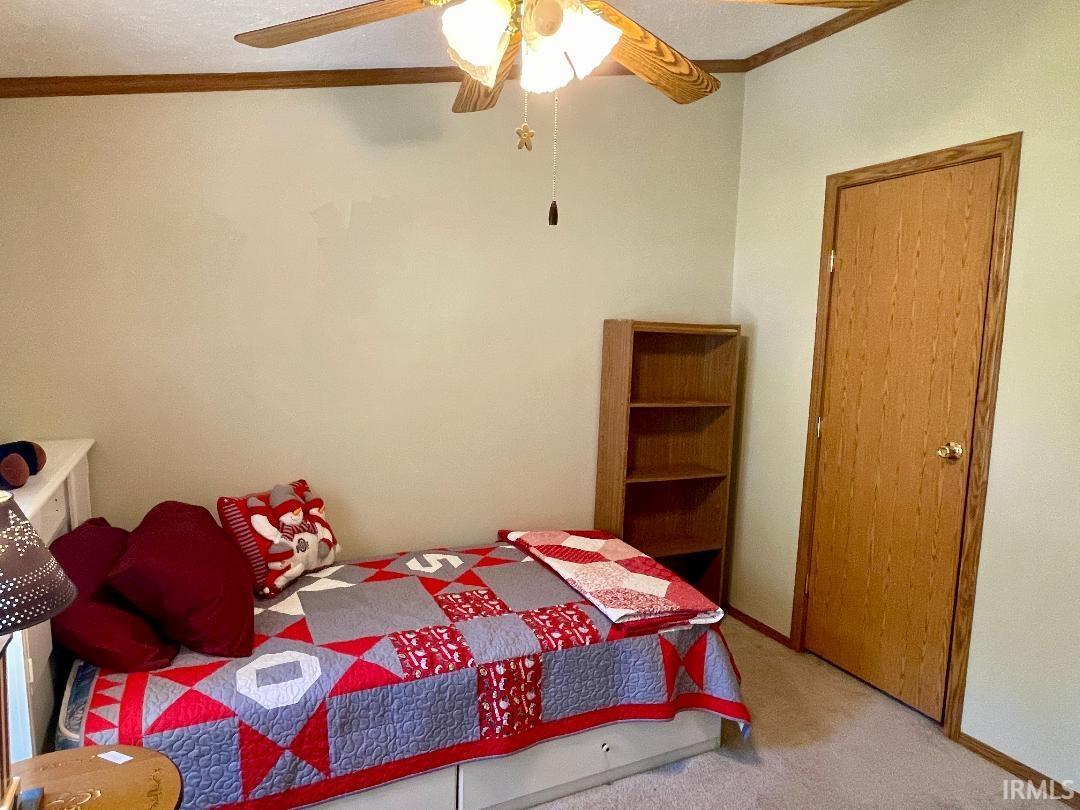 Bedroom featuring a ceiling fan with light fixture, carpeted flooring, and a wood-finish door