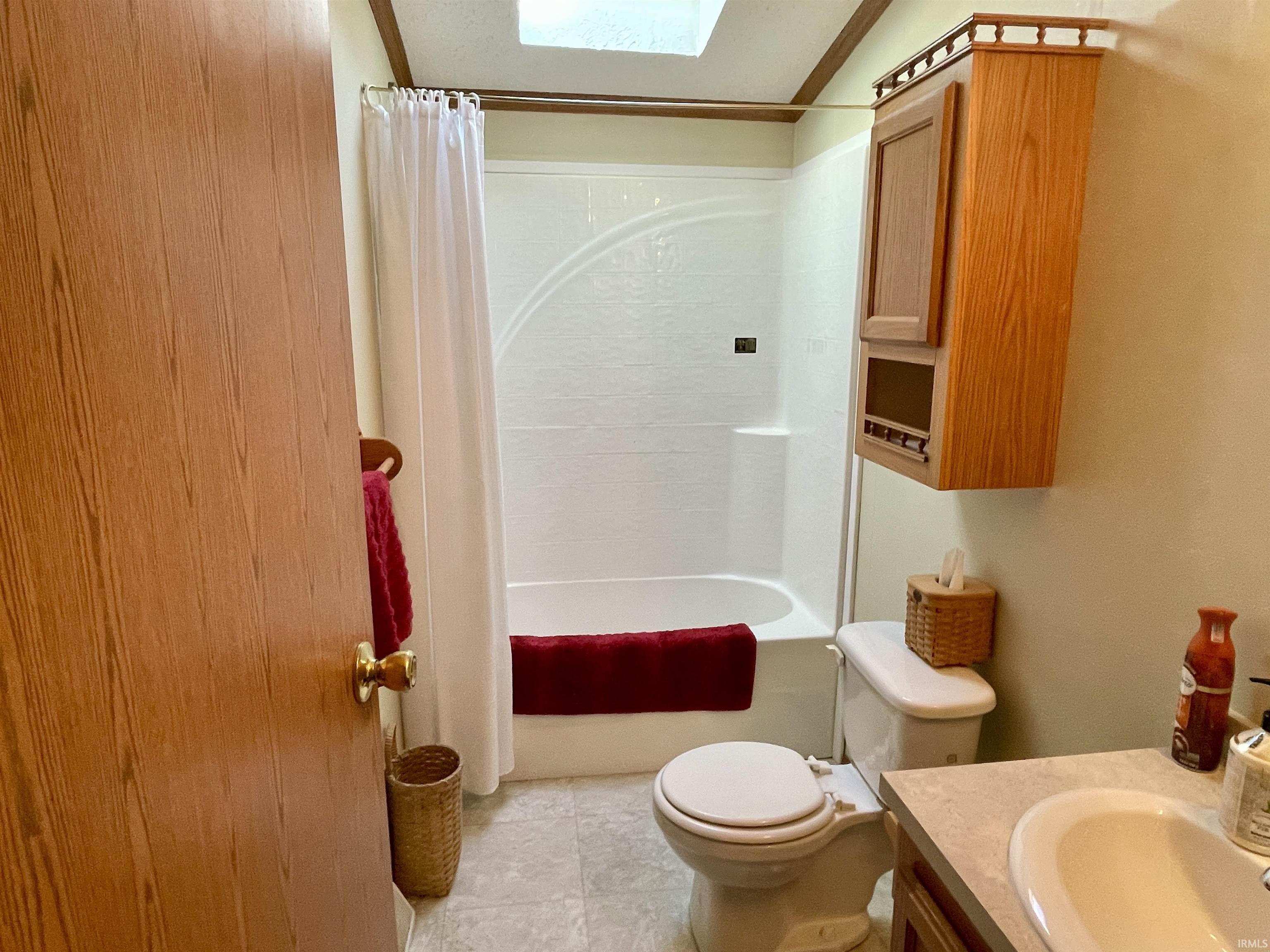 Bathroom featuring a skylight, full bathtub with shower, wall-mounted storage cabinet, and a vanity with an integrated sink