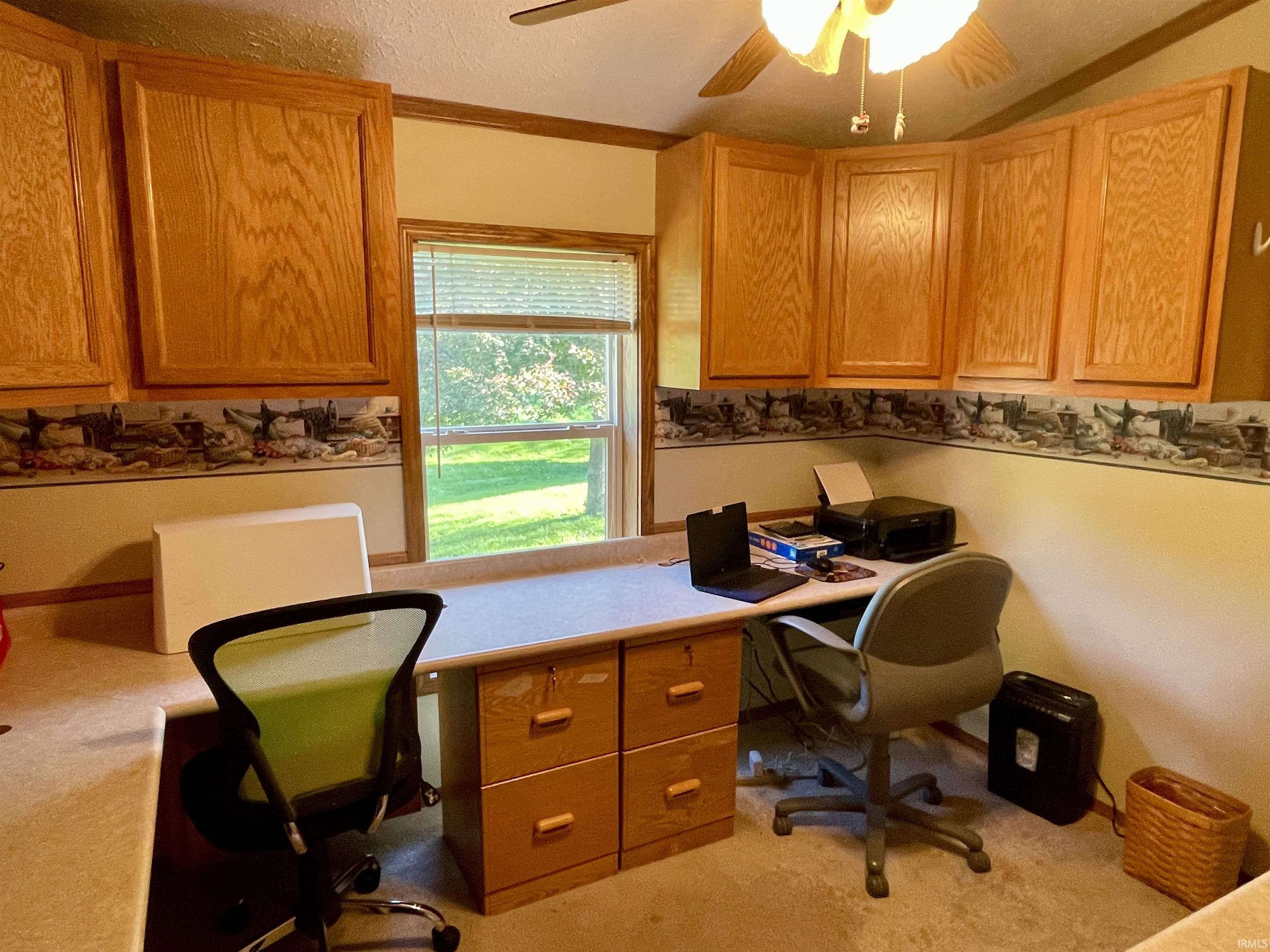 Integrated desk area featuring light-toned countertops, a built-in wood-finish filing cabinet, and overhead wood-finish cabinetry