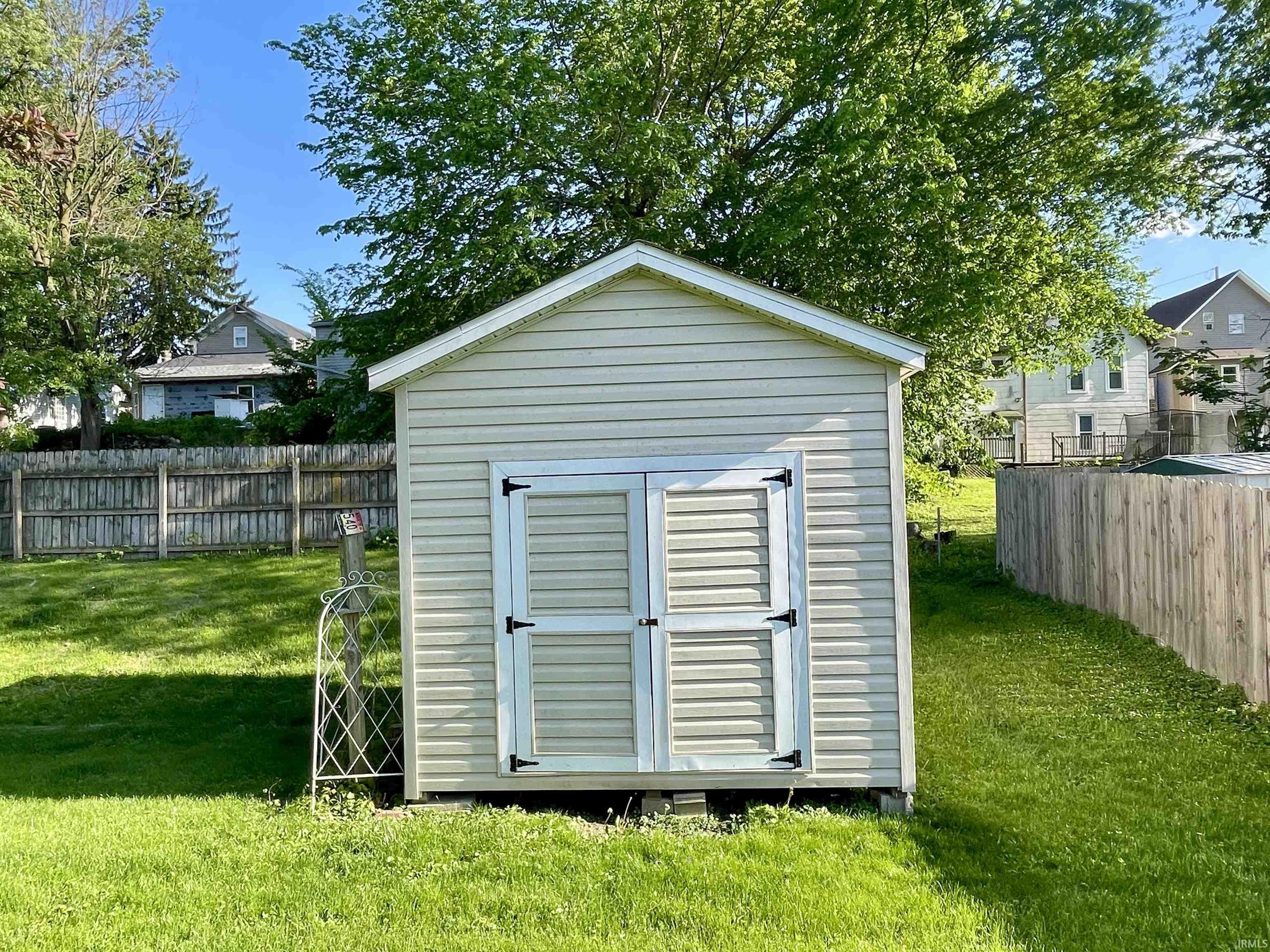Detached storage shed featuring vinyl siding, an A-frame roof, and double doors with black hardware
