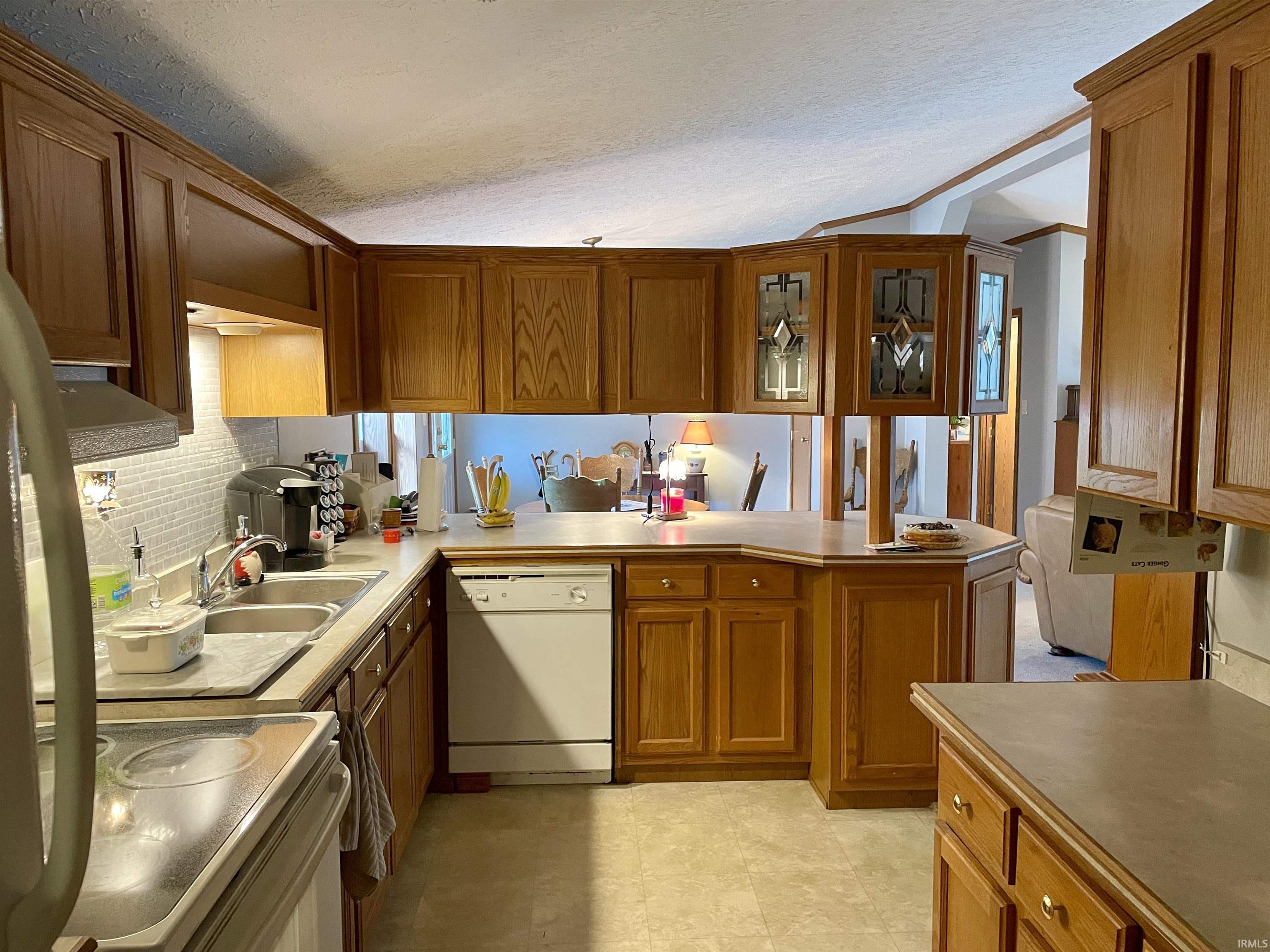 U-shaped kitchen featuring wood-finish cabinetry, a double basin sink, and a white dishwasher