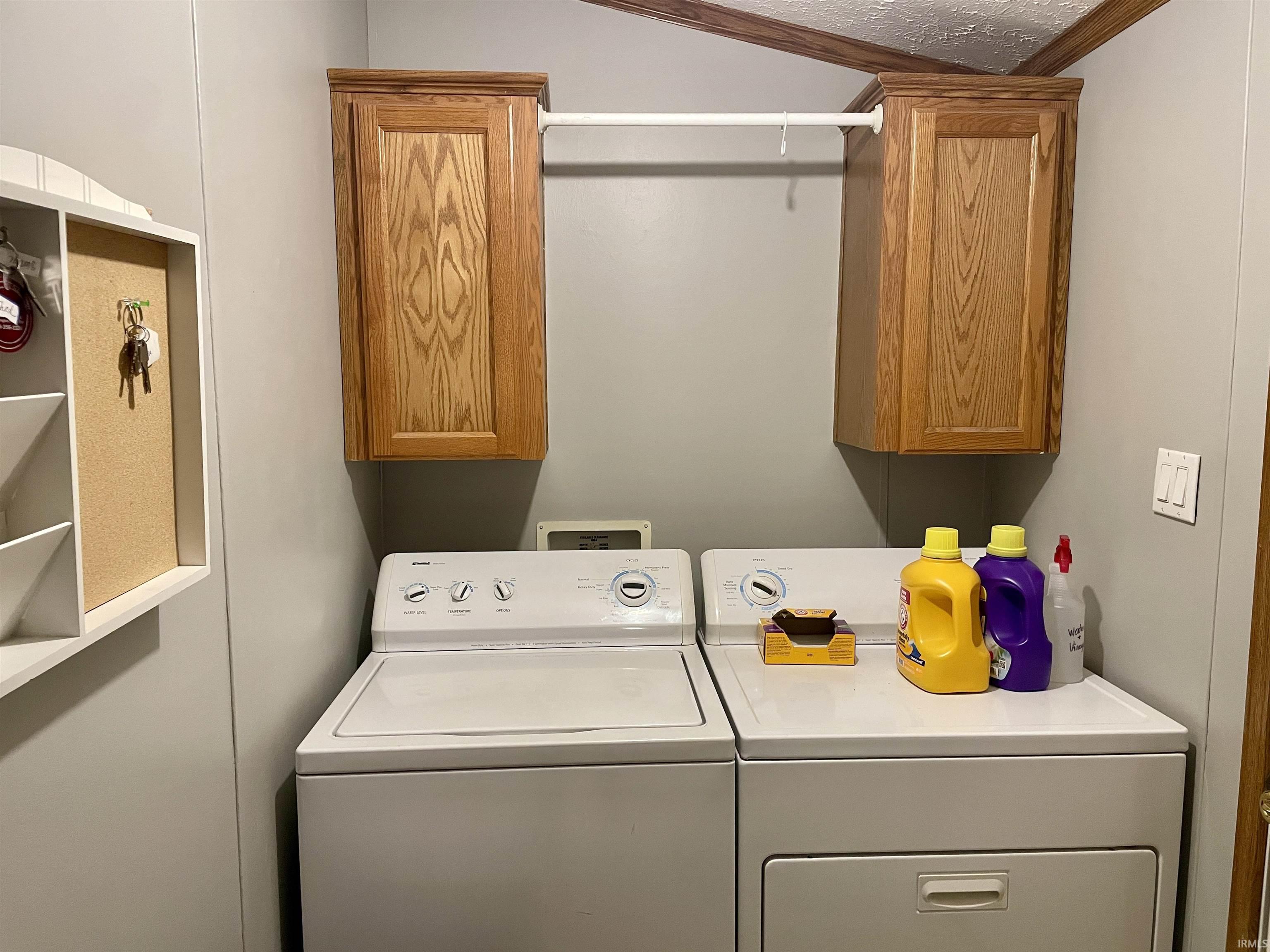 Dedicated laundry area featuring overhead wood-finish cabinetry, a white hanging rod, light gray wall paneling, and a white ceiling with wood-finish trim