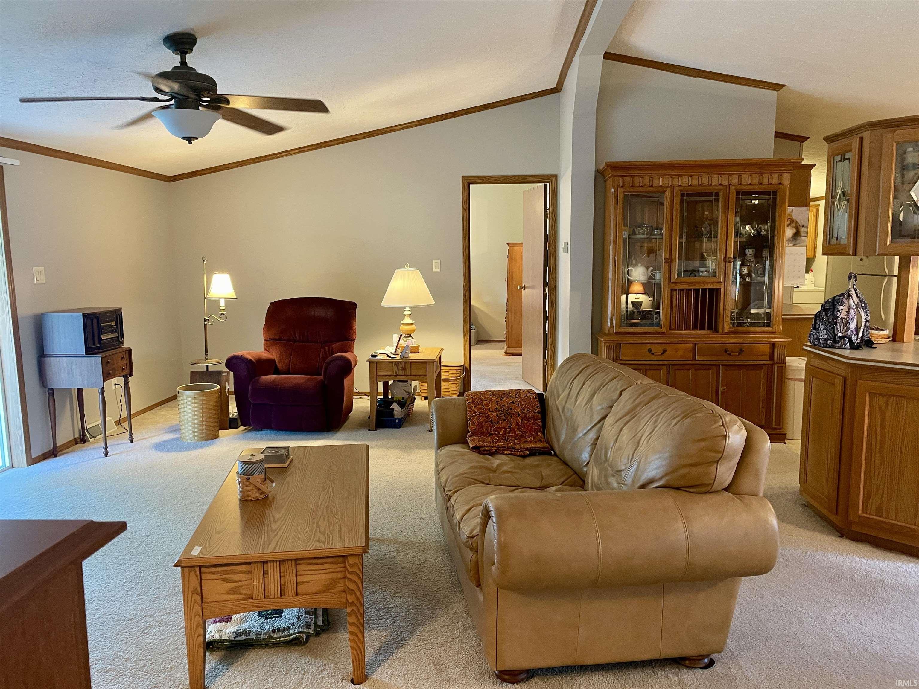 Living area featuring vaulted ceilings, crown molding, a ceiling fan with integrated lighting, and carpeted flooring