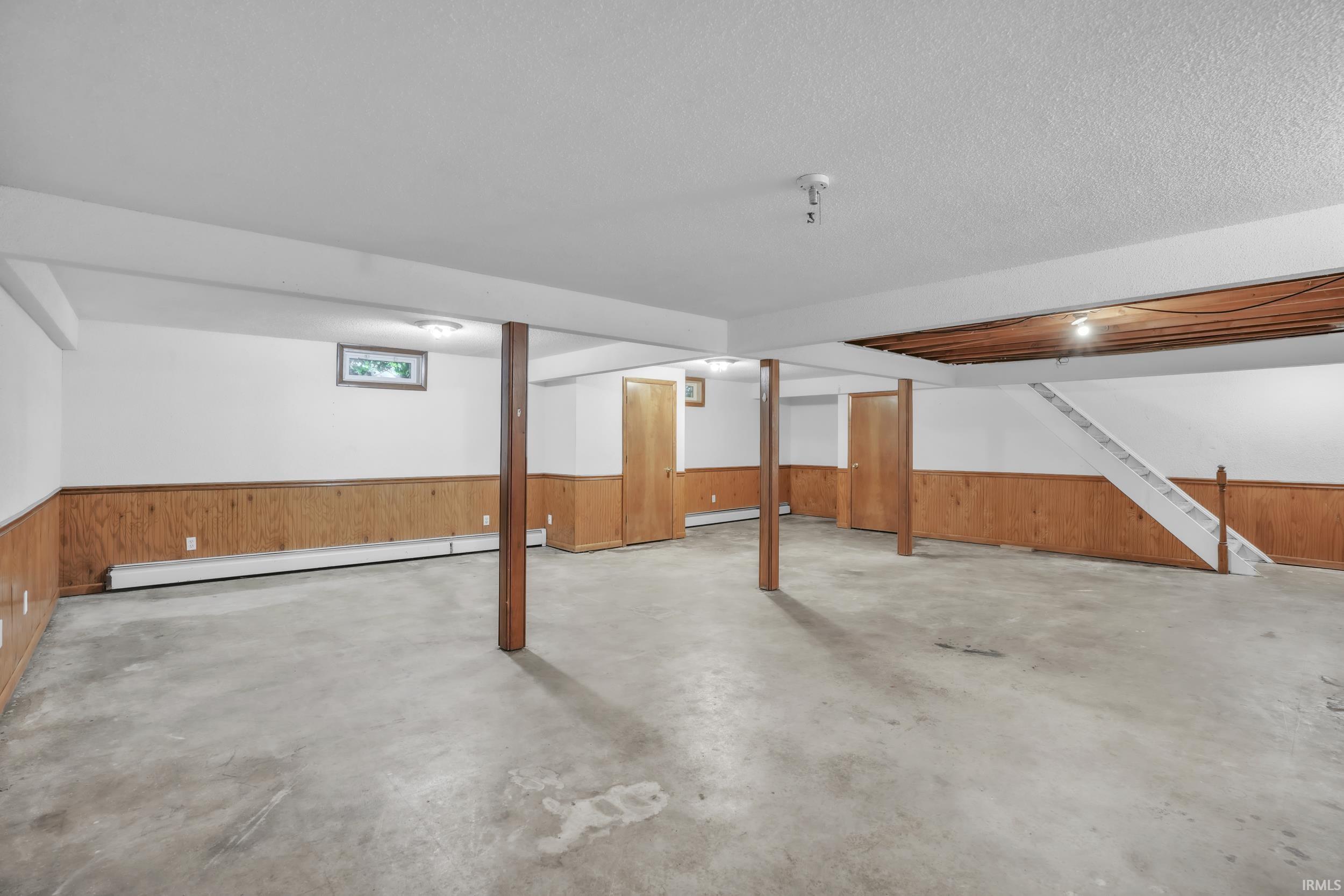 Expansive basement space featuring concrete flooring, wood paneling, and a white painted staircase