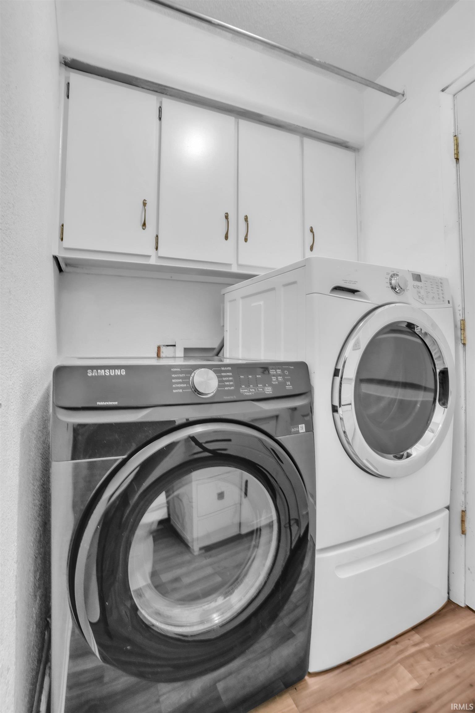 Dedicated laundry space featuring wood-finish flooring and white upper cabinetry with brass-toned hardware
