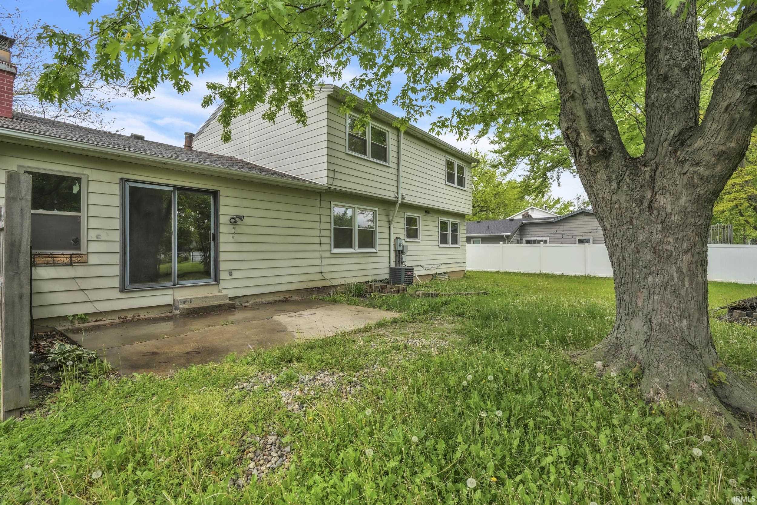 Expansive rear yard featuring mature trees, a white privacy fence, and a concrete patio