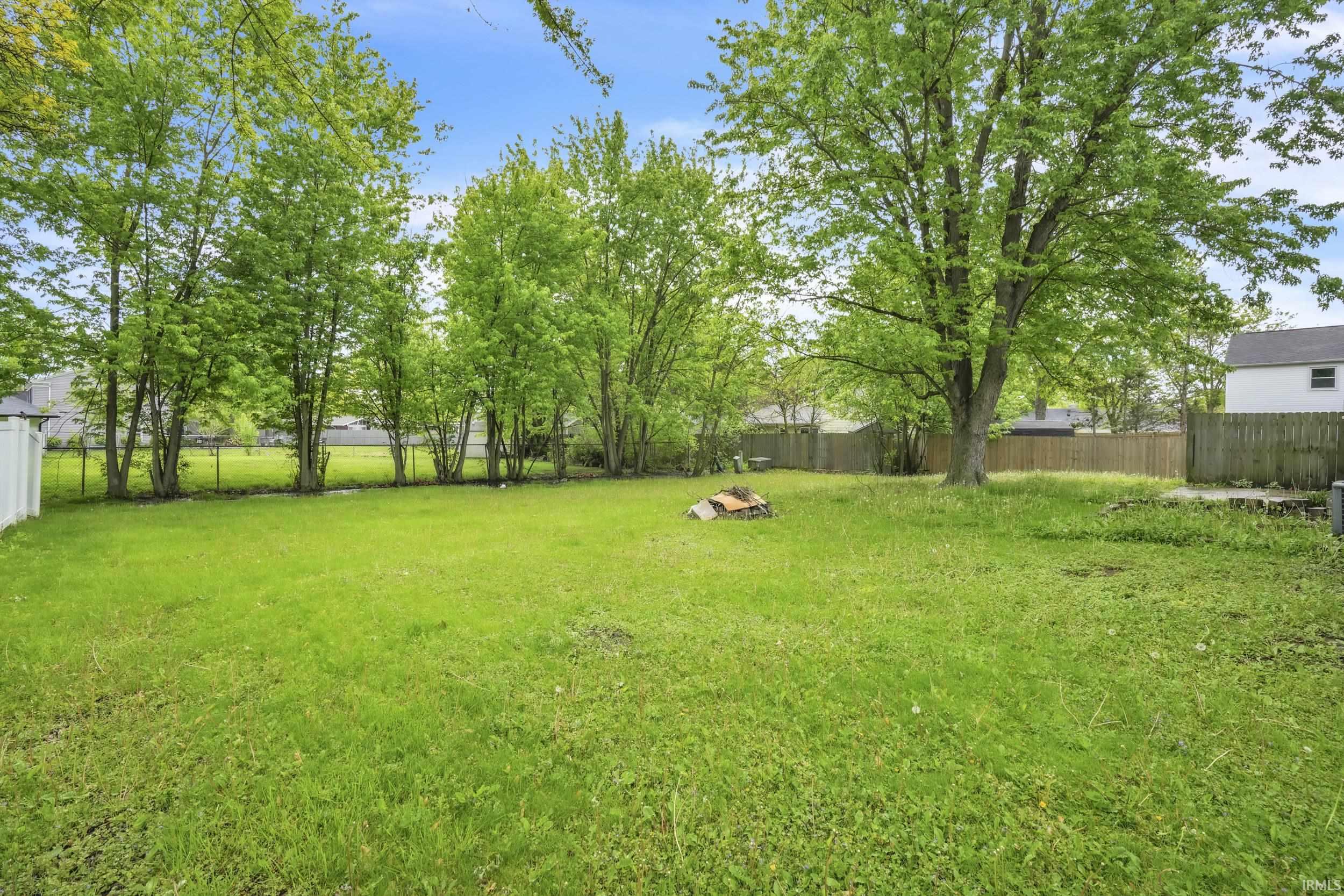 Expansive green lawn with mature trees and a partial wood privacy fence