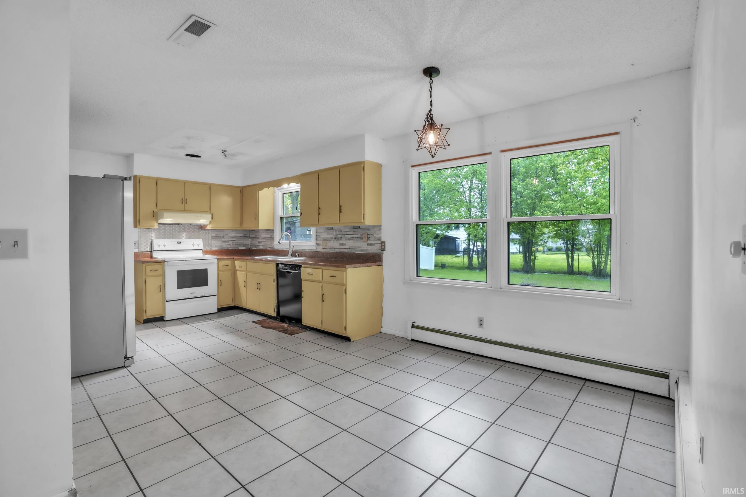 Spacious kitchen and dining area featuring white tile flooring, a tile backsplash, ample cabinetry, and two large windows