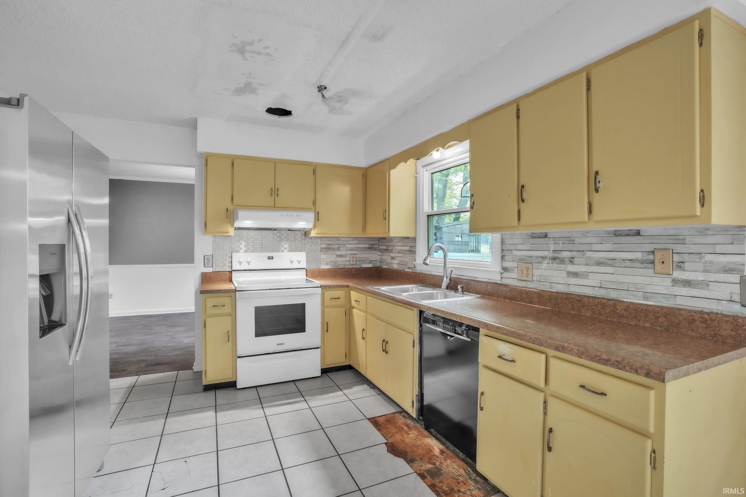 Kitchen featuring yellow cabinetry, white tile flooring, stainless steel refrigerator, white electric range, and dark-finish countertops