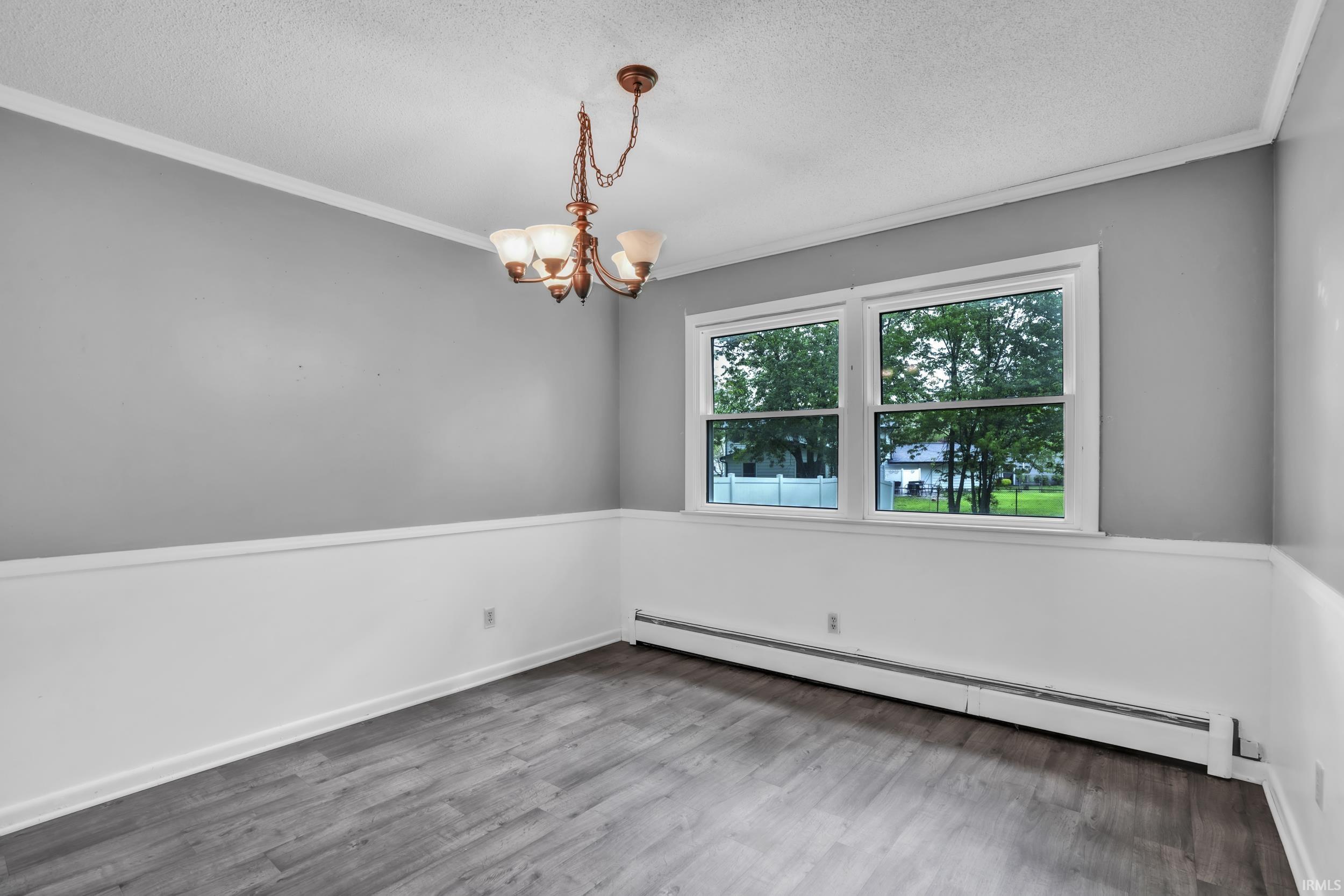 Room featuring wood-finish flooring, two-tone wall paneling with a light gray upper and white lower, and a multi-light chandelier