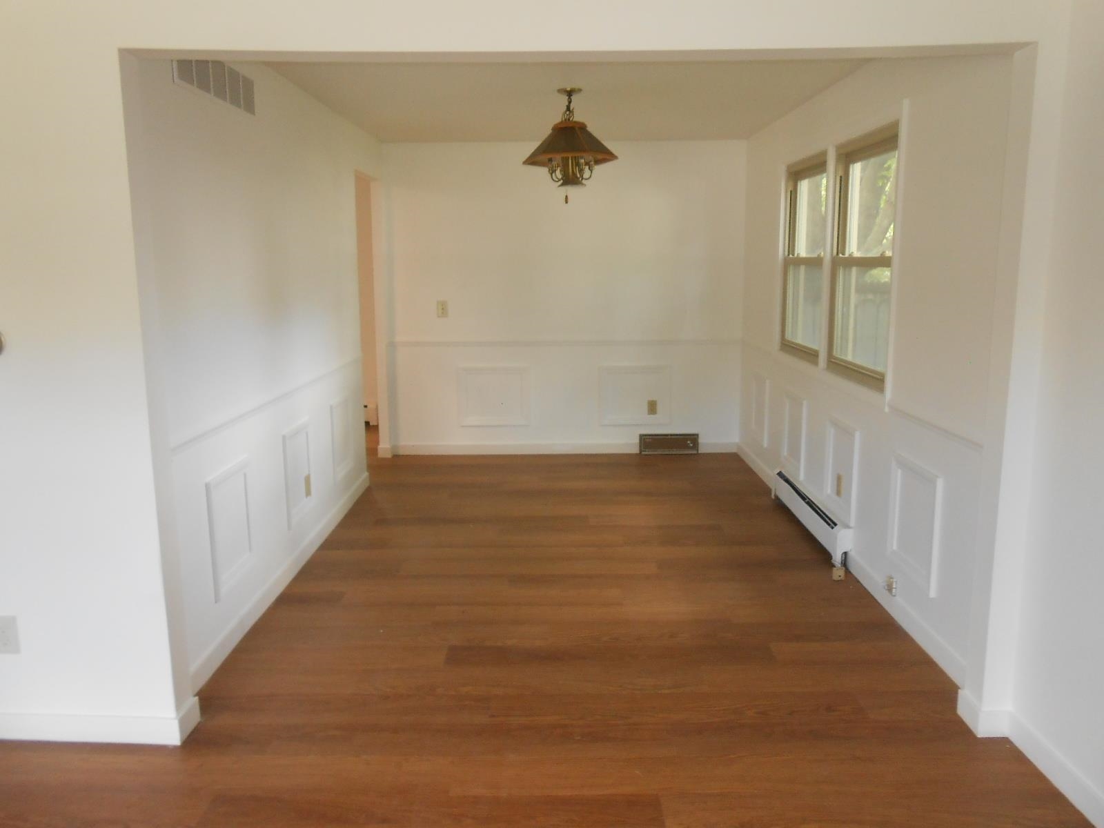 Spacious interior room featuring wood-finish flooring, white panel molding, and two windows