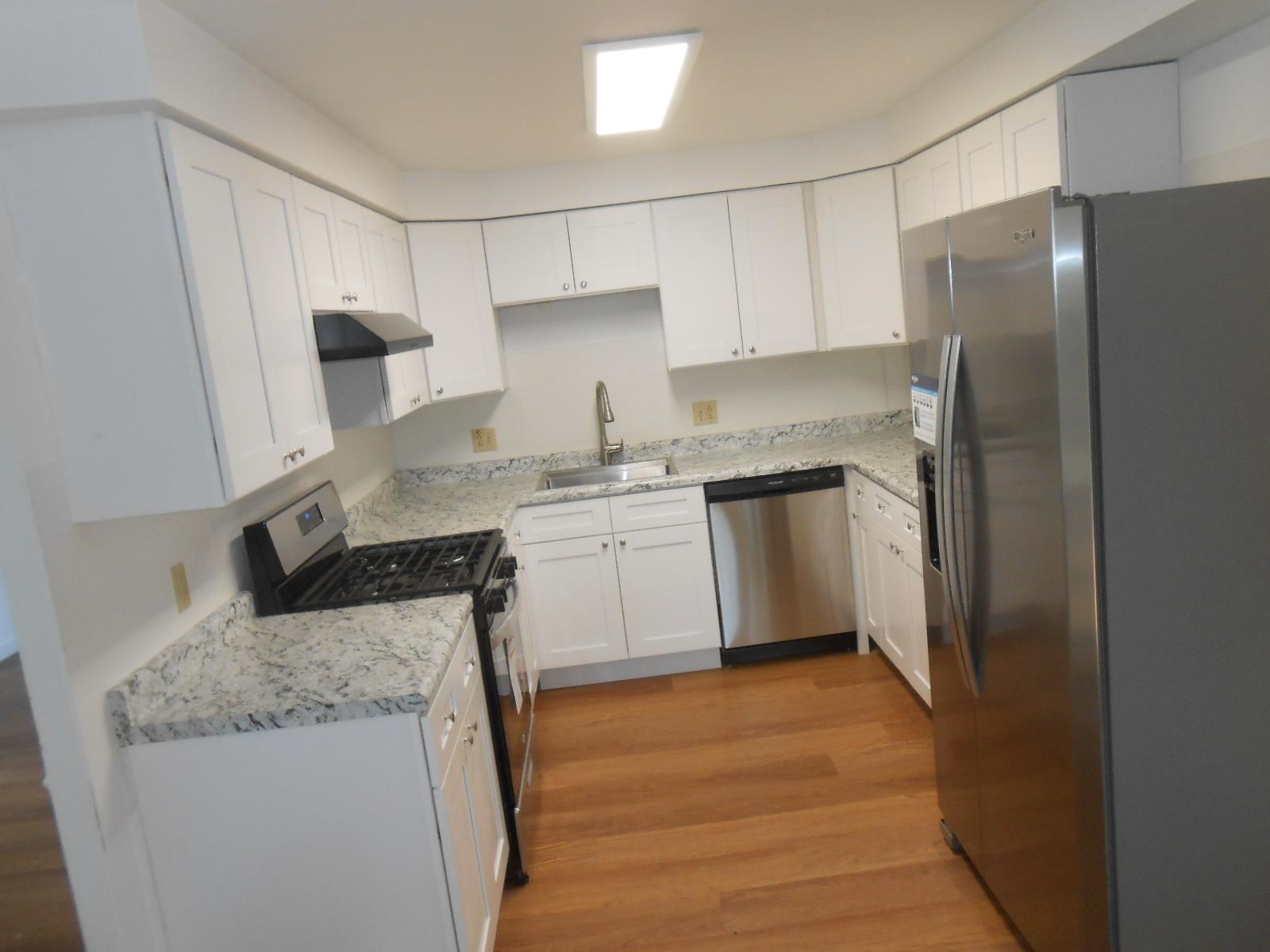 U-shaped kitchen featuring white cabinetry, light-toned countertops, and wood-finish flooring