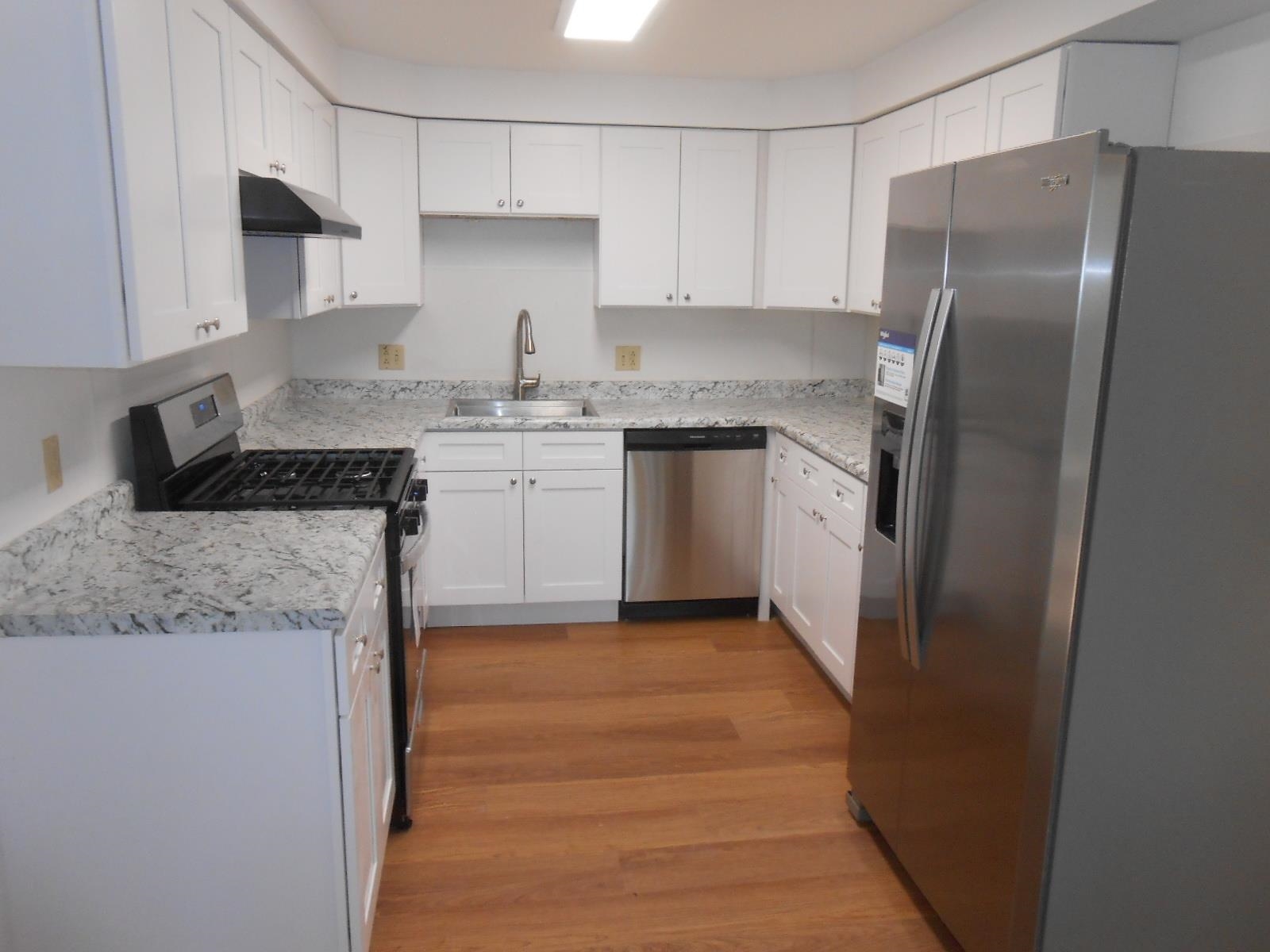 Kitchen featuring white shaker-style cabinetry, light-toned countertops with a speckled pattern, stainless steel appliances, and wood-finish flooring