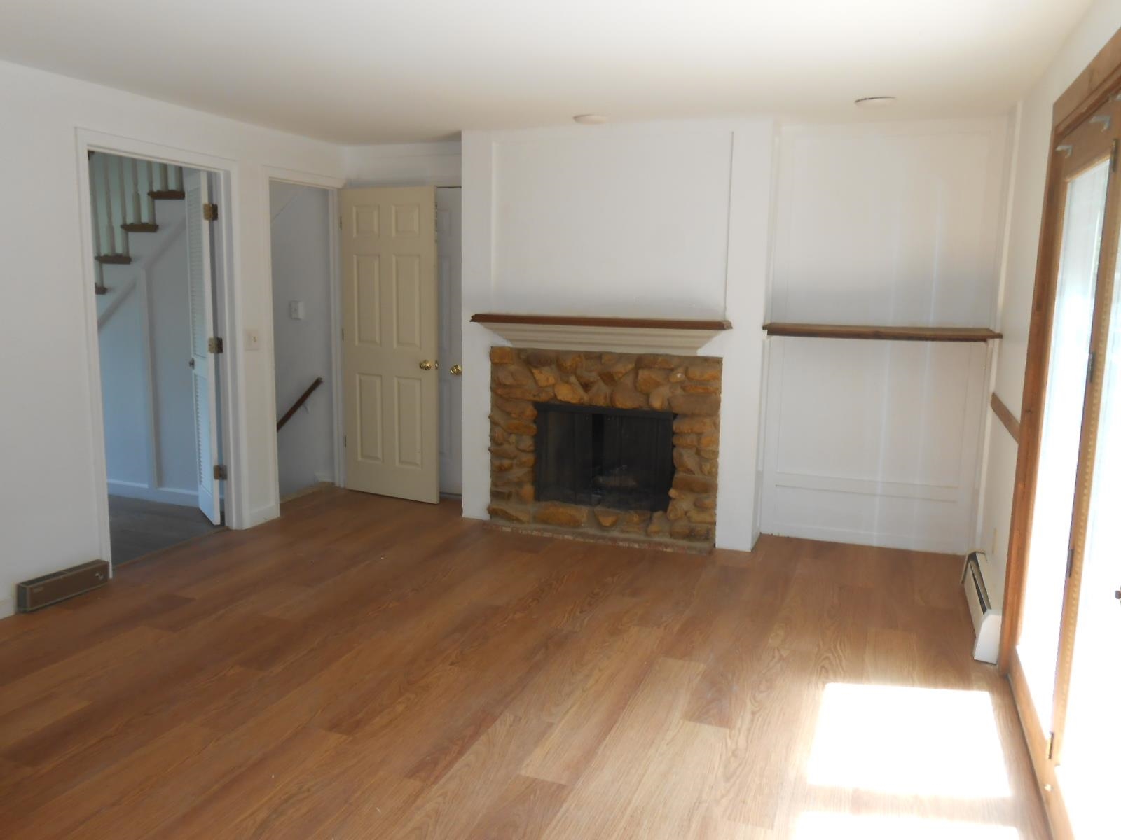 Living area with wood-finish flooring, a stone-faced fireplace with a wooden mantel, and a built-in wooden shelf
