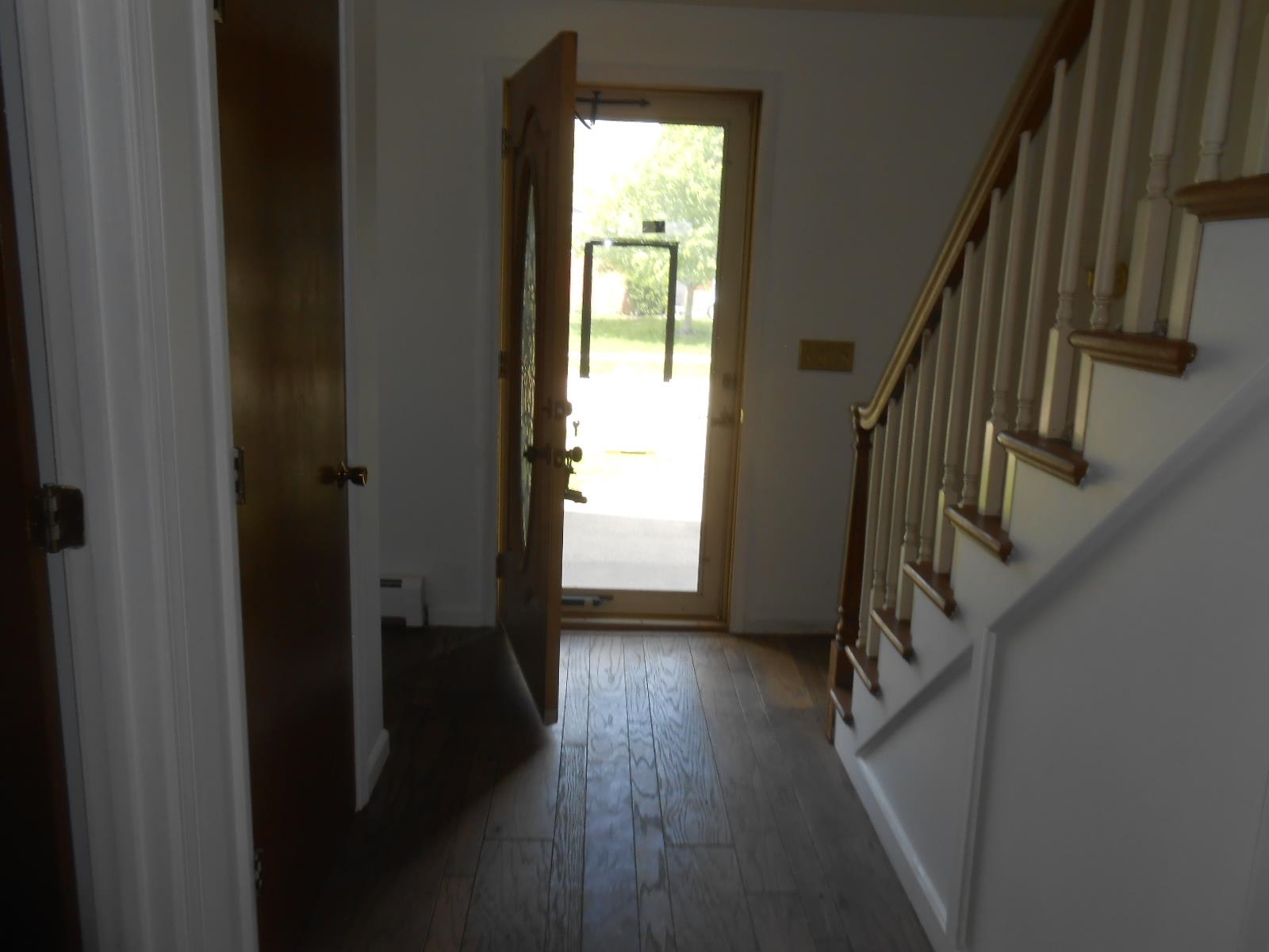Entryway featuring wood-finish flooring, a wood-paneled door with decorative glass, and a traditional staircase with turned spindles and a wood handrail