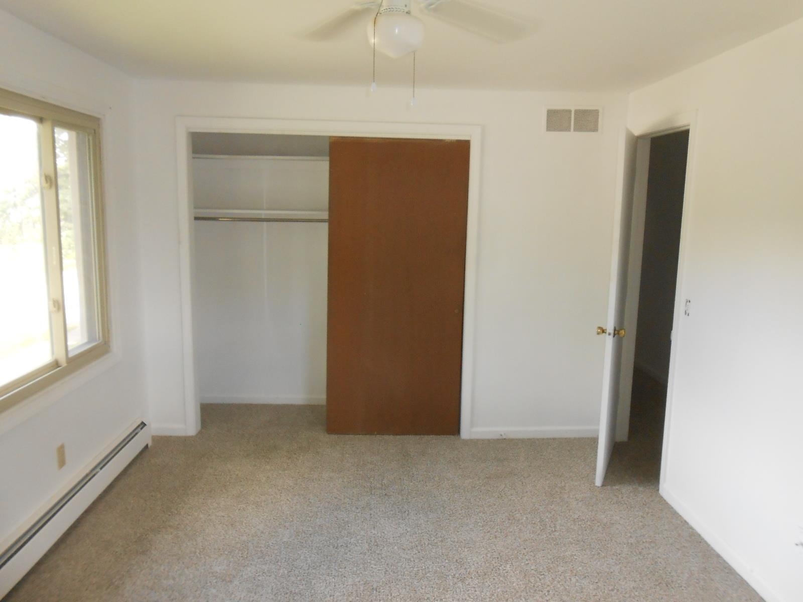 Carpeted room featuring a ceiling fan, a window with exterior views, baseboard heating, a bifold closet door, and a white interior door