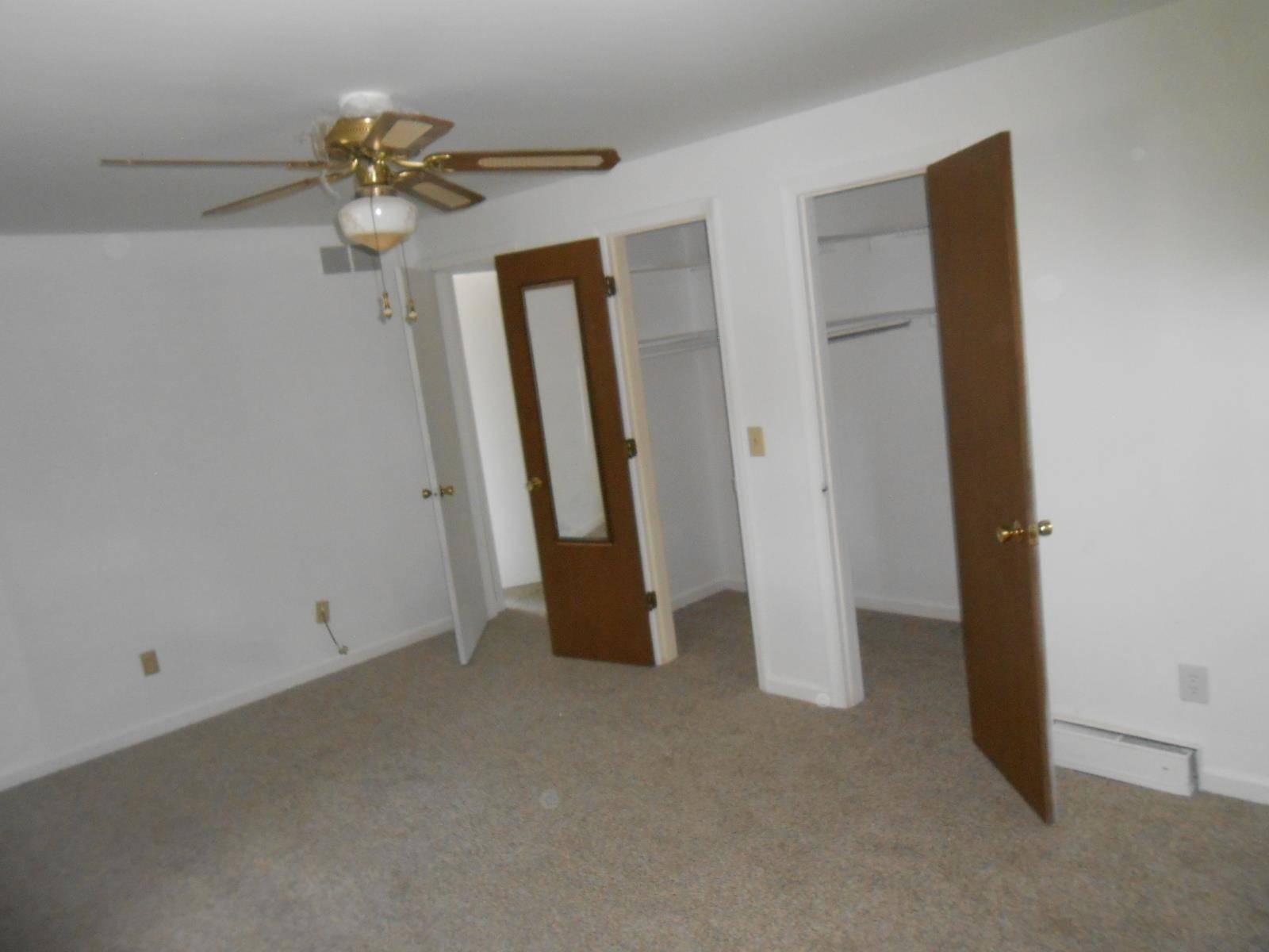 Carpeted room featuring a ceiling fan, two built-in closets with shelving, and a solid door with a full-length mirror