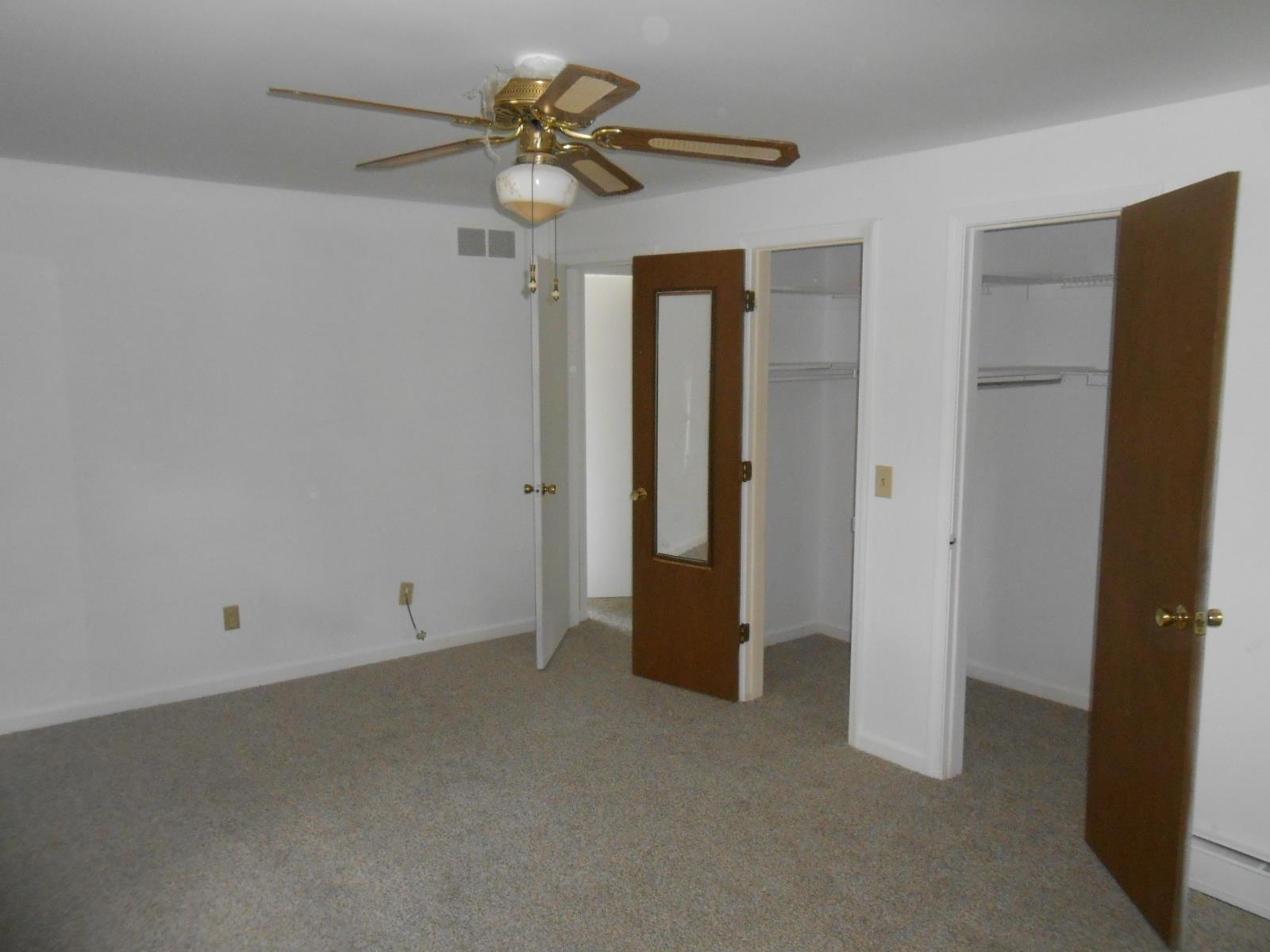 Carpeted room featuring a ceiling fan with light fixture, multiple closets with shelving, and white walls