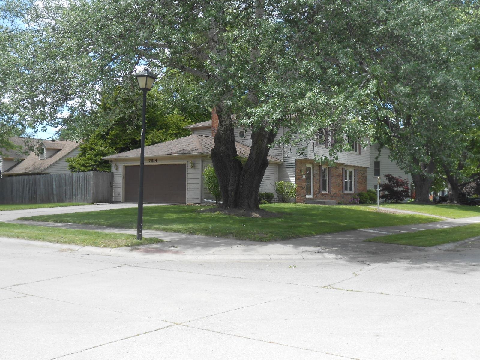 Two-story residence featuring siding and brick accents, a two-car attached garage, and mature trees providing natural shade