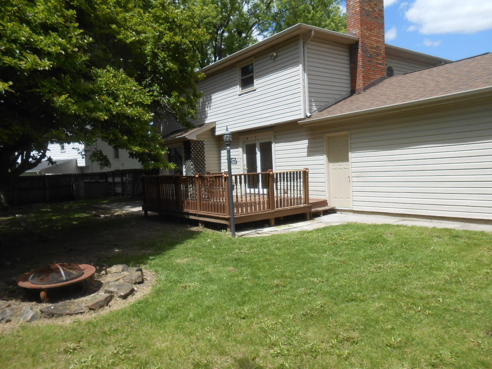 Rear exterior featuring a wooden deck with railing, sliding glass door access, and a brick chimney