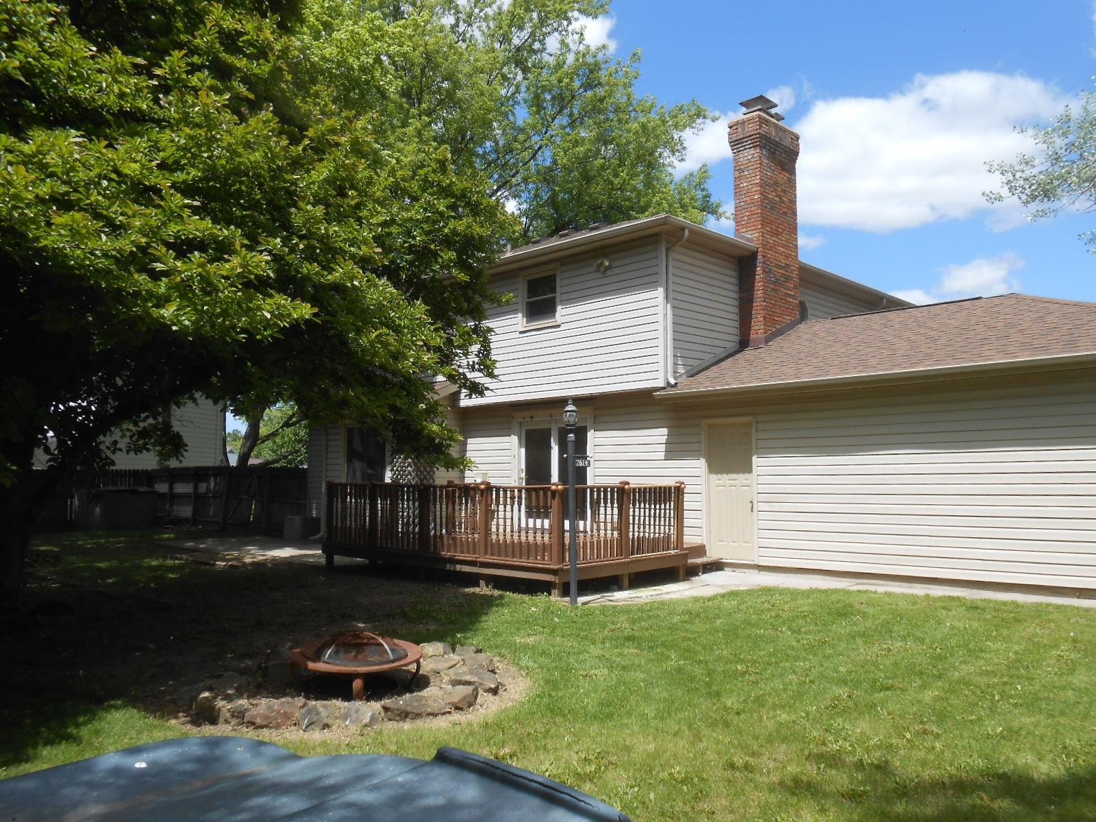 Backyard featuring a wood deck with railing, a grass lawn, and a stone-ringed fire pit