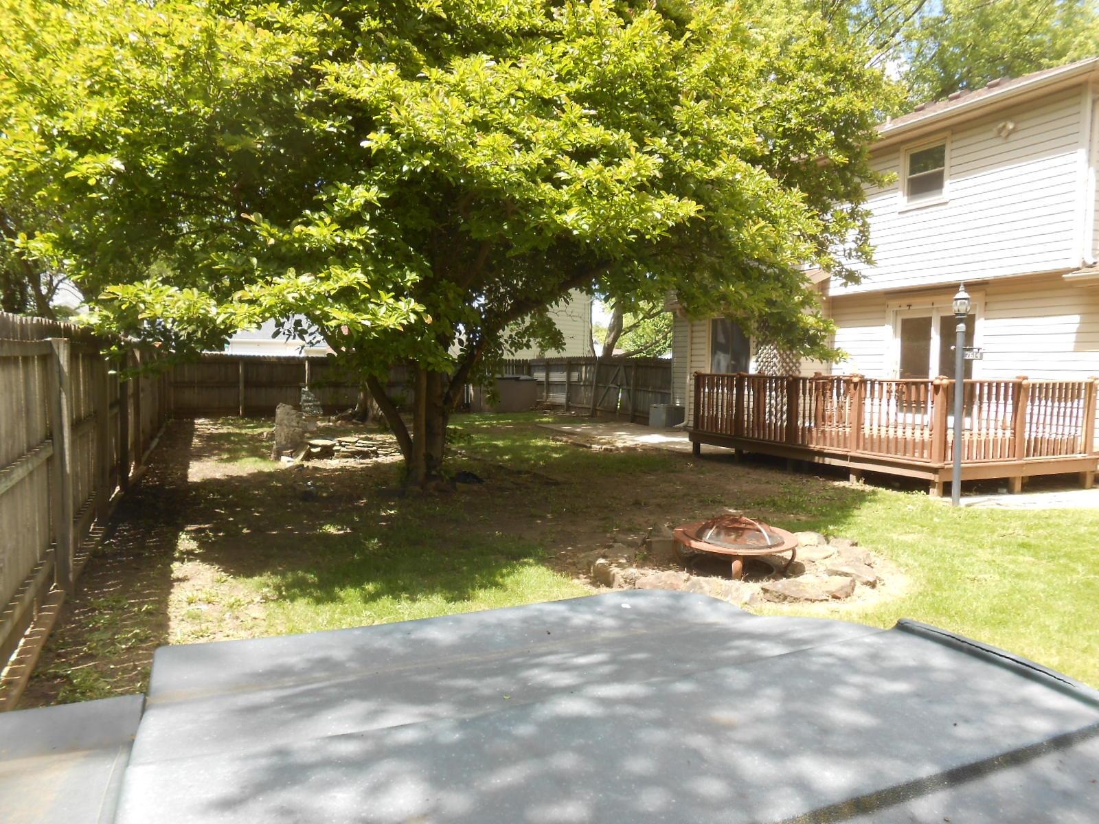 Expansive fenced backyard featuring a wood deck, mature trees, a fire pit, and a grassy area