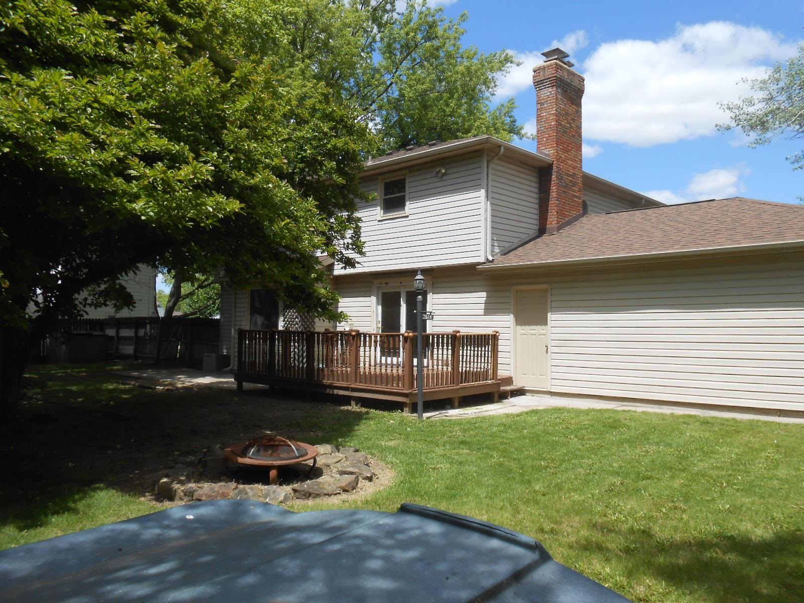 Expansive backyard featuring a wood deck, red brick chimney, and mature trees