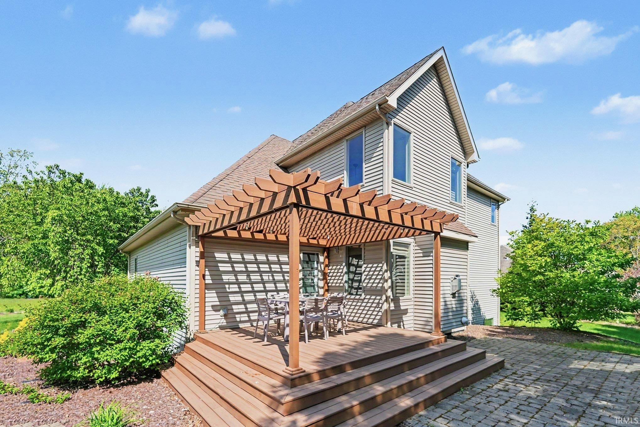 Multi-level wood-finish deck with a pergola, stone paver patio, and mature landscaping