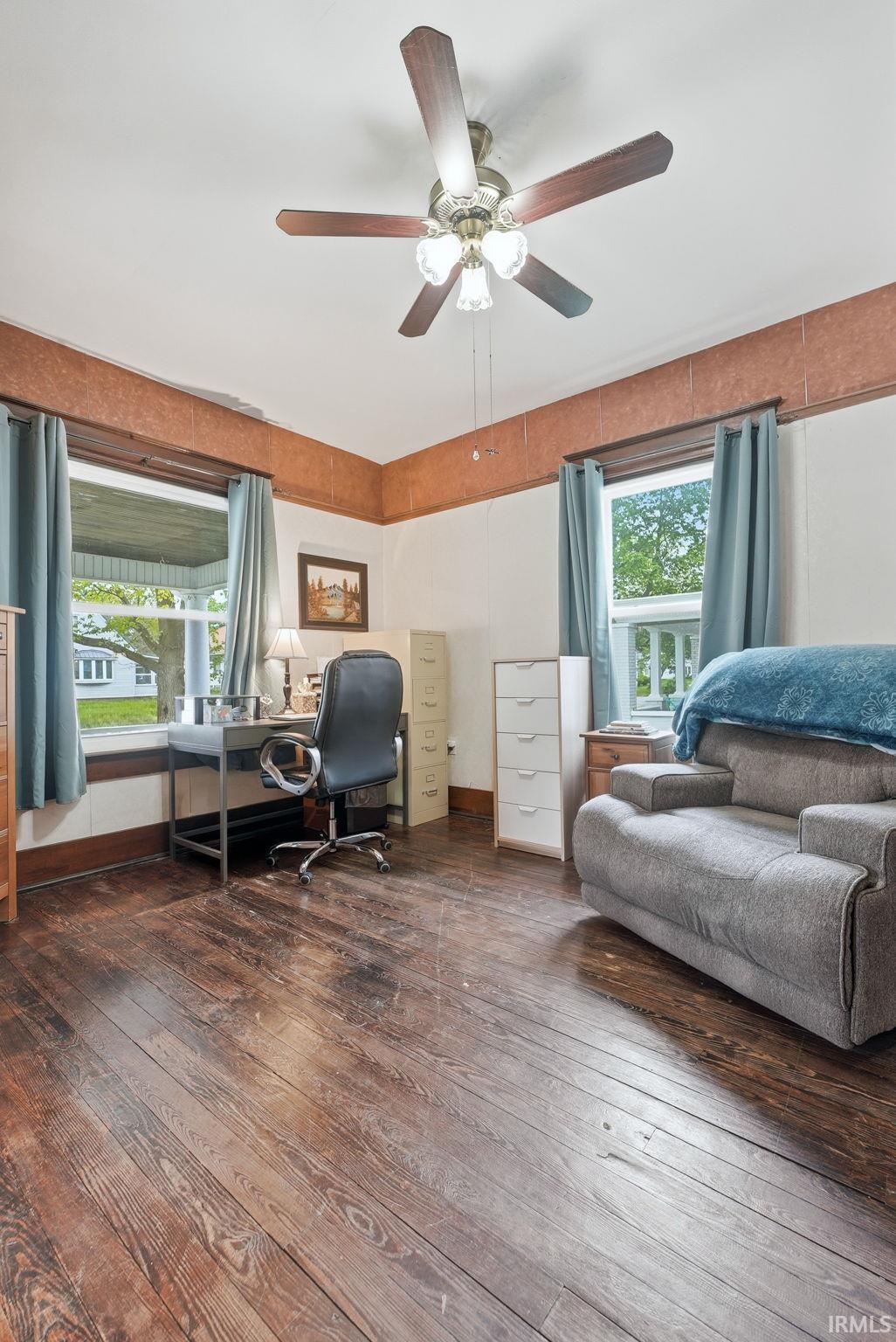 Room featuring wood-finish flooring, two windows with trim, a ceiling fan with integrated lighting, and crown molding