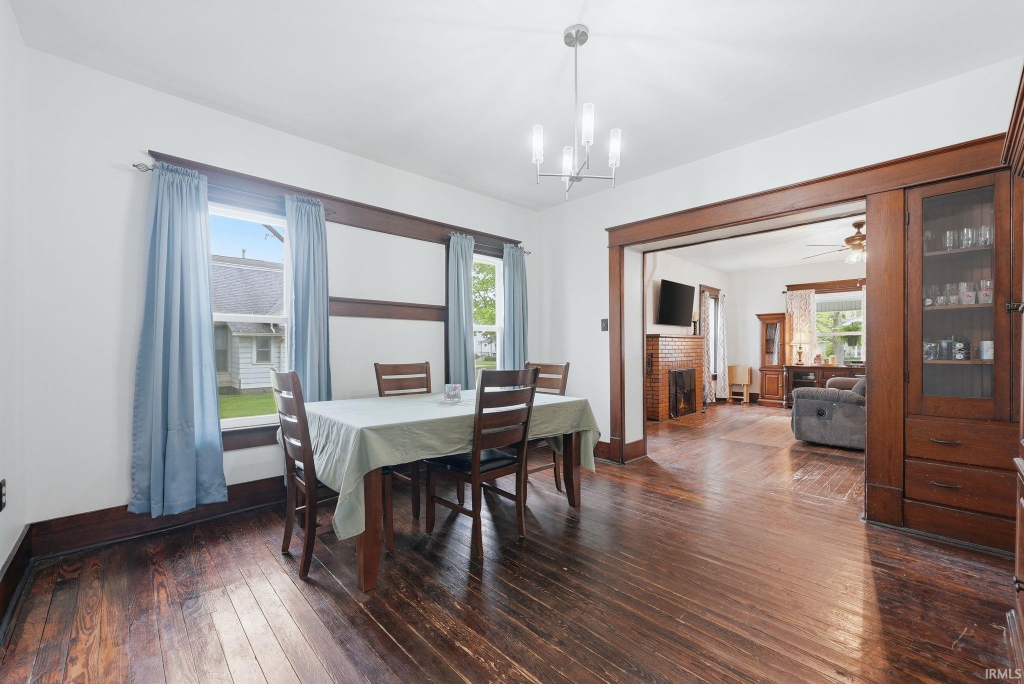 Dining area featuring dark wood-finish flooring, two windows with white trim, and a contemporary chandelier